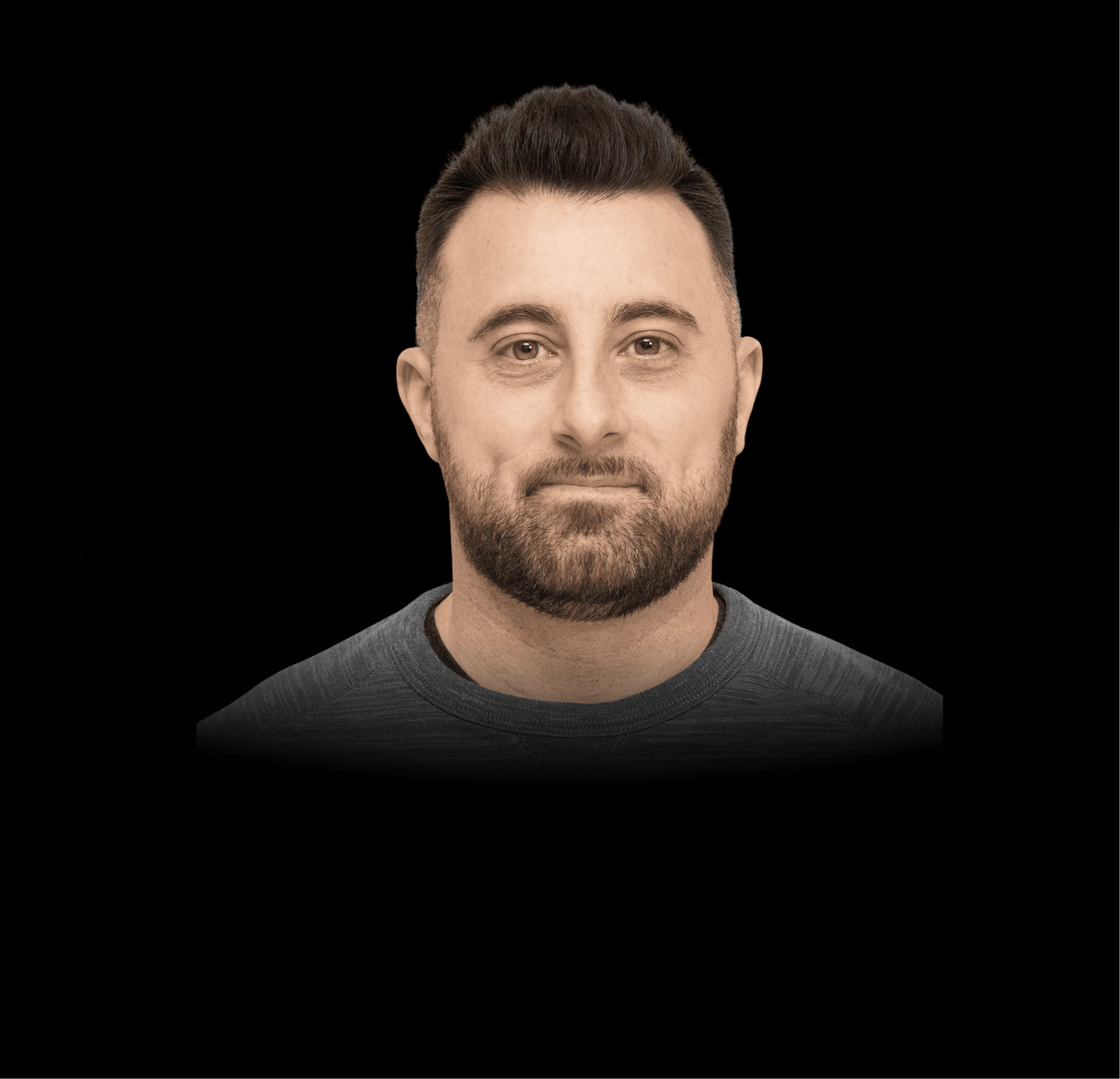 Portrait of a man with short dark hair and beard wearing a grey shirt against a black background.