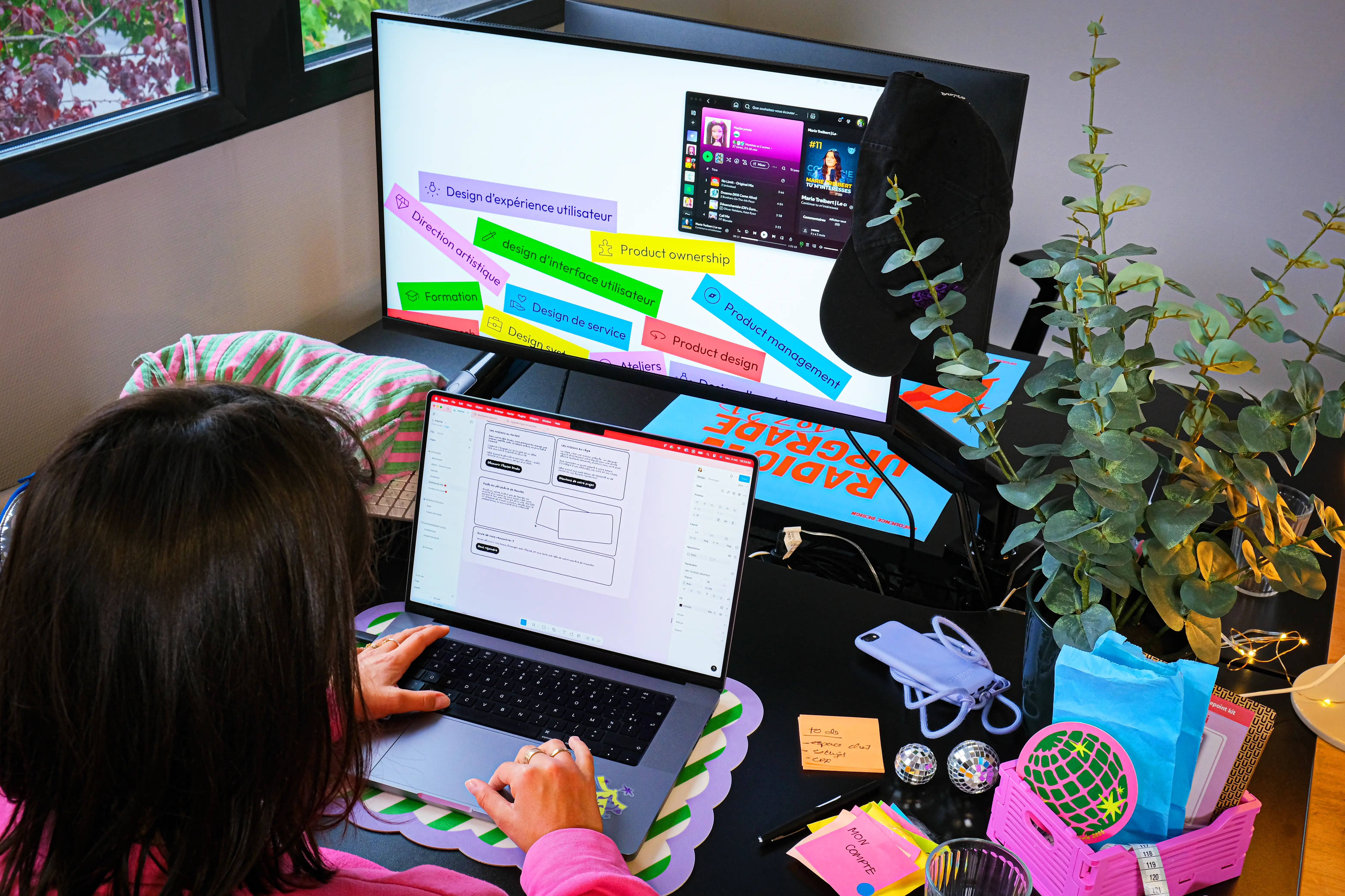 Une Product Designer de notre agence design UX UI Nantes Lyon Paris travaillant sur l'interface UI et le flux utilisateur UX sur double écran, avec des mots-clés de spécialisation affichés à l'écran.