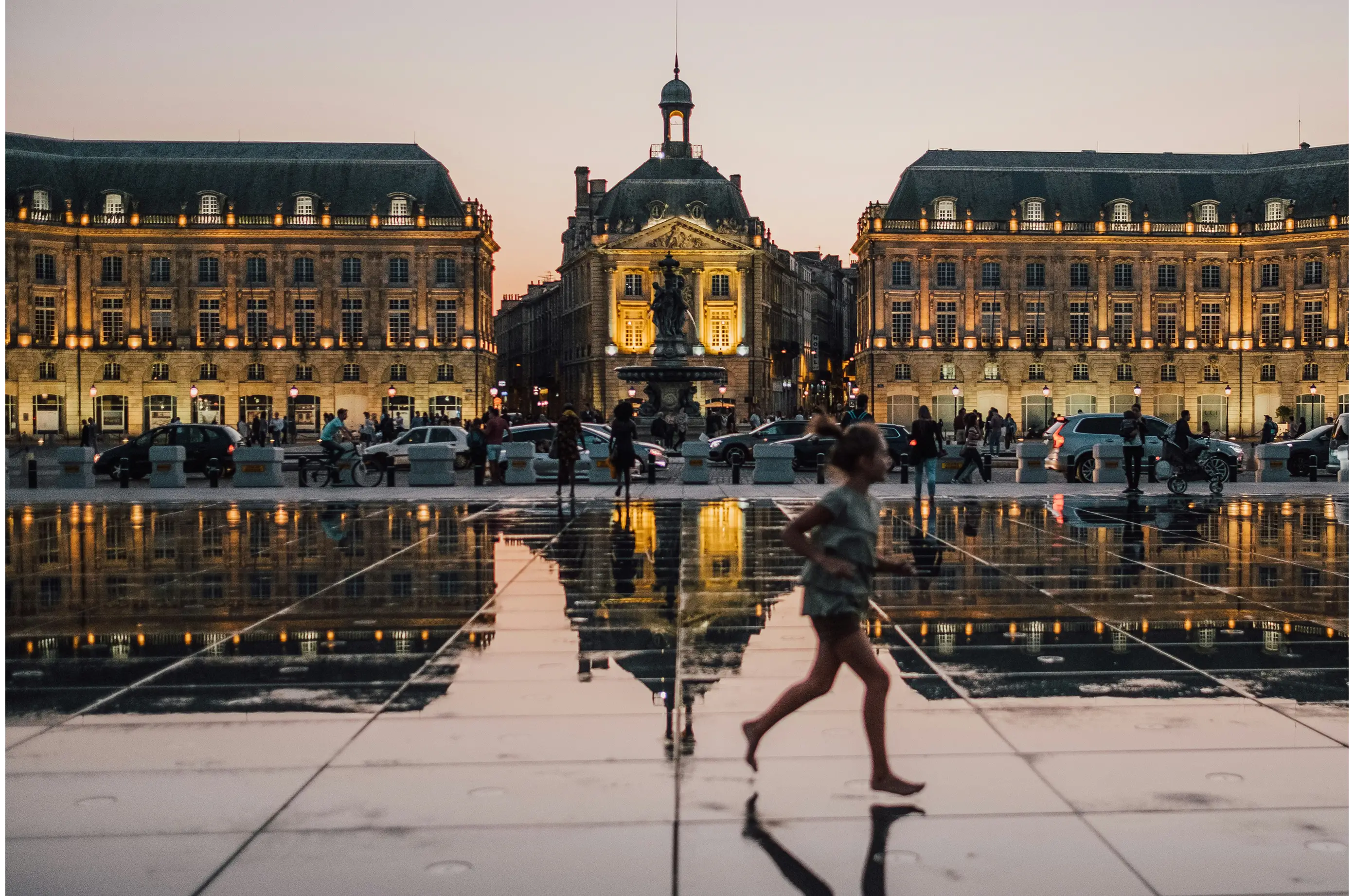 Vue iconique du Miroir d'Eau et de la Place de la Bourse à Bordeaux au coucher du soleil, symbolisant l'ancrage local de l'agence.