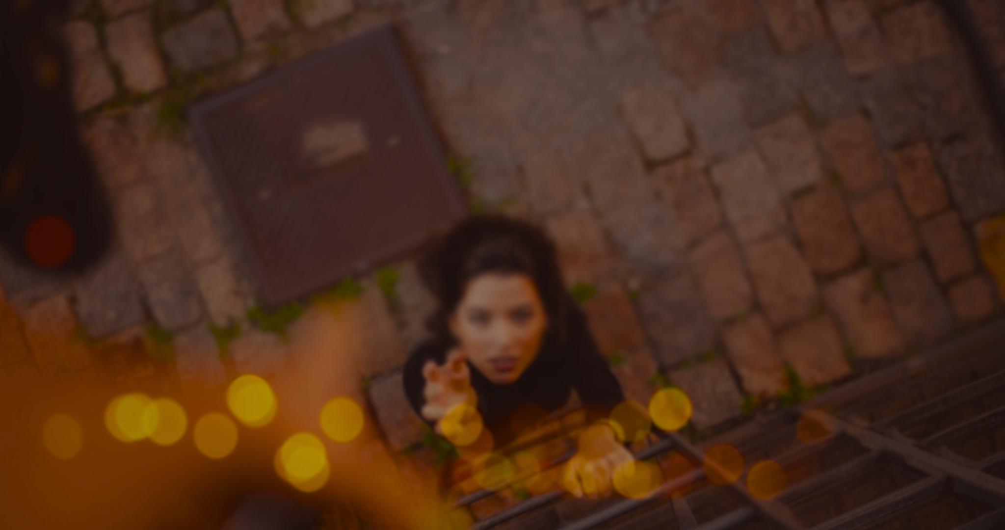 Blurred overhead view of a woman reaching upwards while climbing a metal ladder on a cobblestone street.