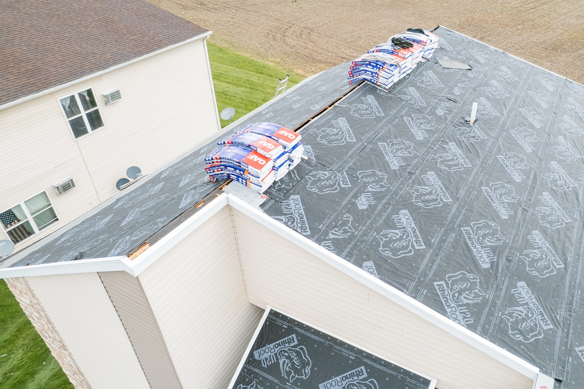 Close-up of a brown shingle roof with damaged and lifted shingles revealing underlying black layer.