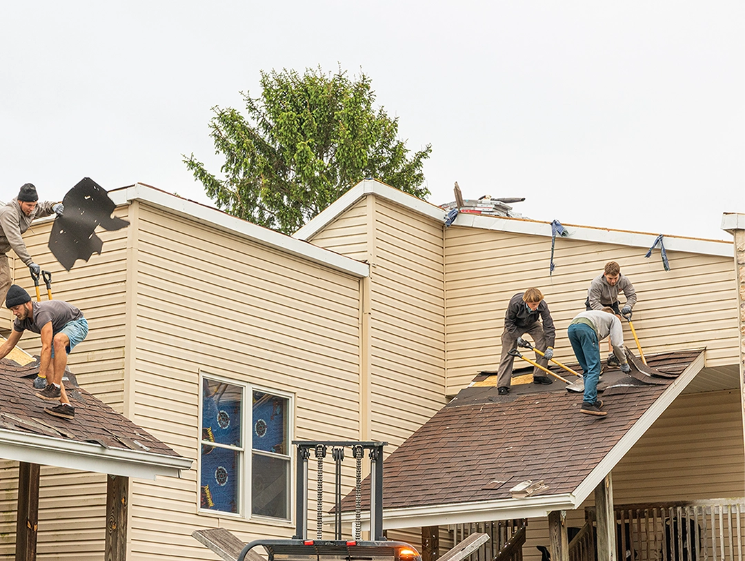 Close-up of a brown shingle roof with damaged and lifted shingles revealing underlying black layer.