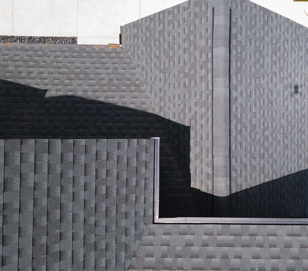 Close-up of a brown shingle roof with damaged and lifted shingles revealing underlying black layer.