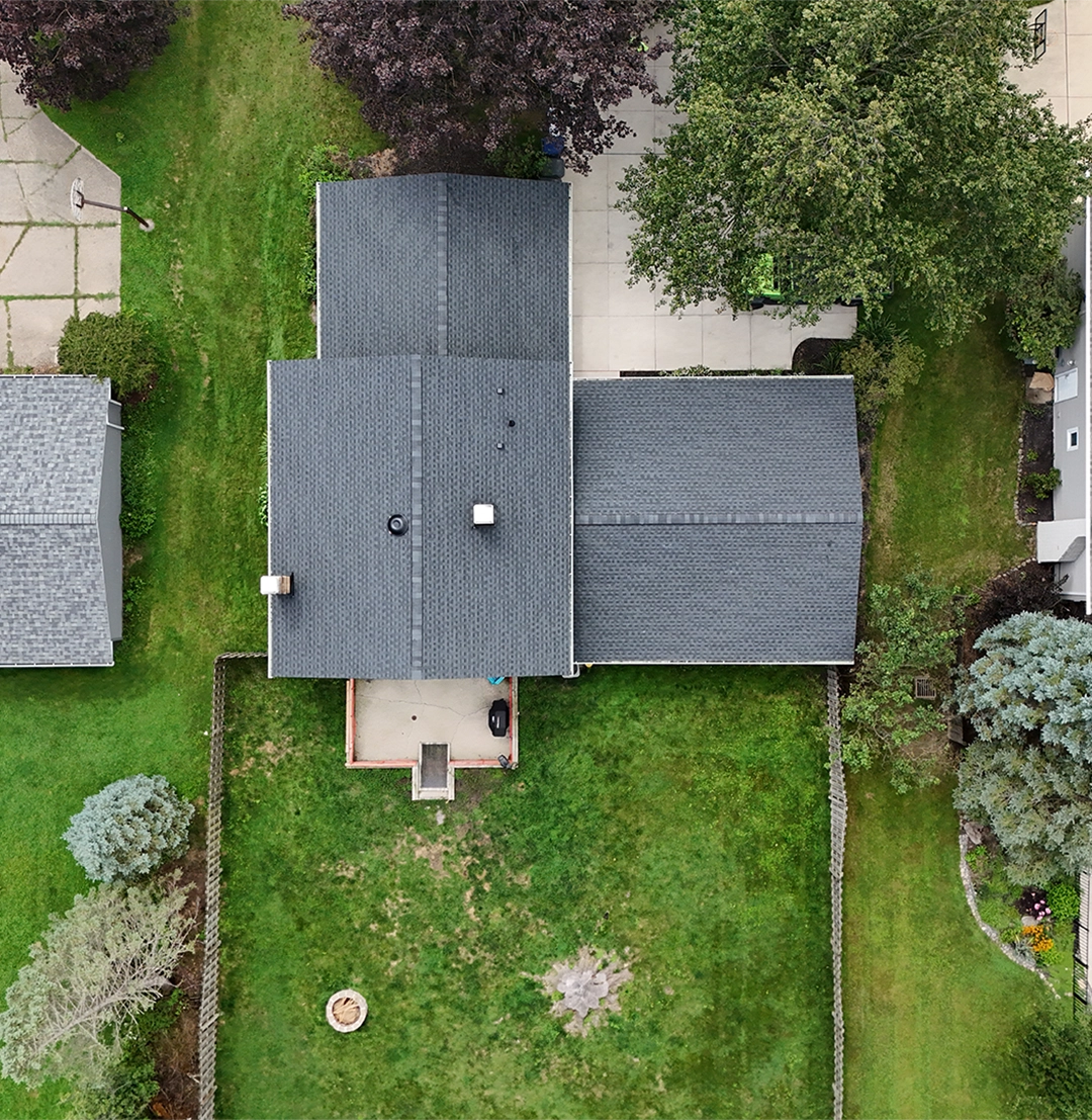 Close-up of a brown shingle roof with damaged and lifted shingles revealing underlying black layer.