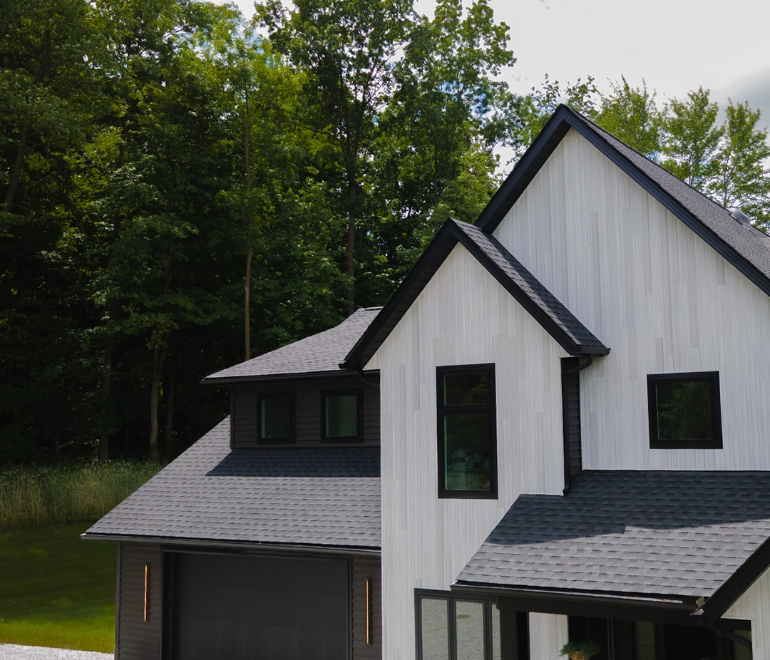 Close-up of a brown shingle roof with damaged and lifted shingles revealing underlying black layer.