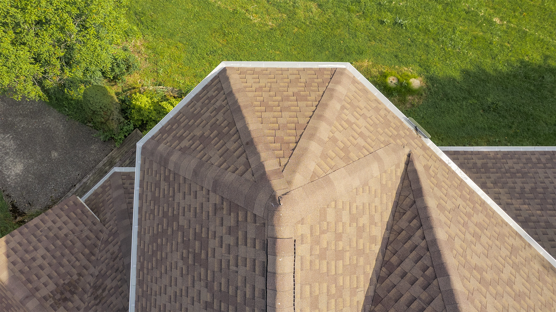 Straight-down drone view of a brown shingle roof with white seamless gutters running along the eaves.