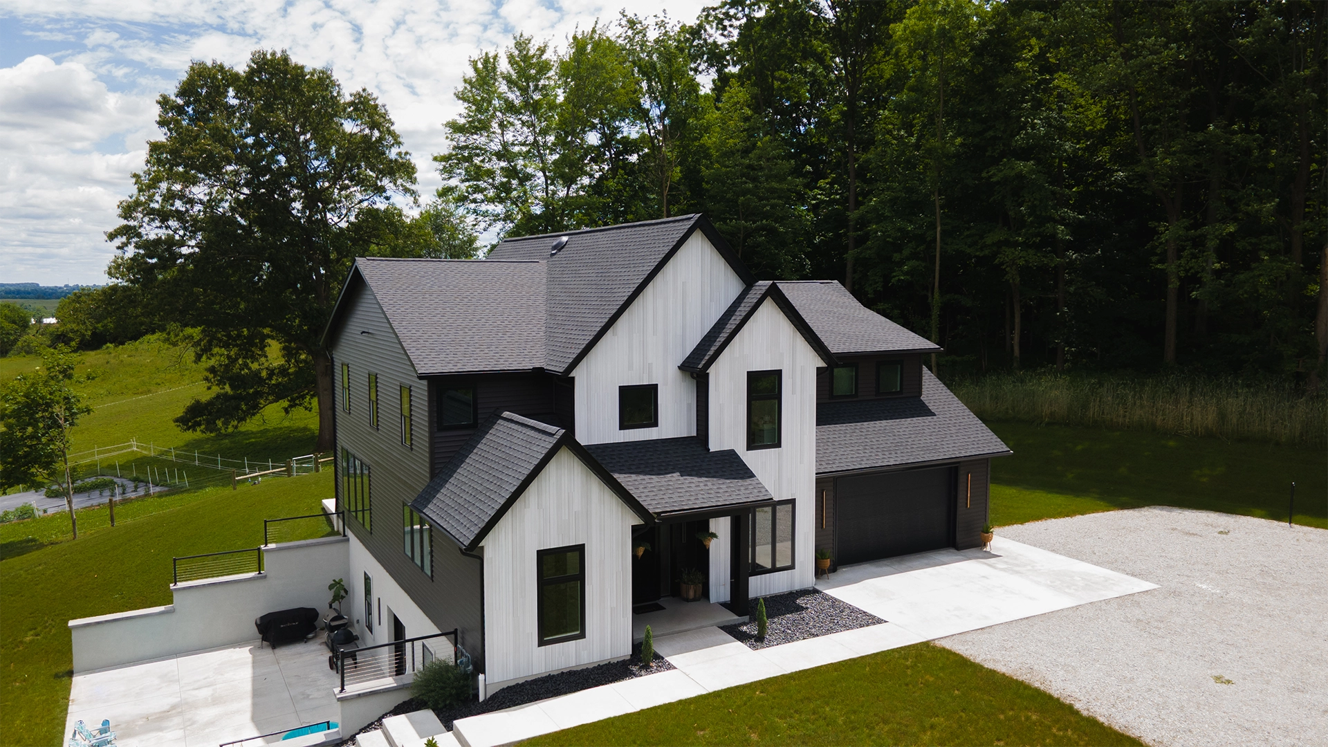 Aerial view of a modern farmhouse with white vertical board-and-batten siding, dark lap siding, and black trim.