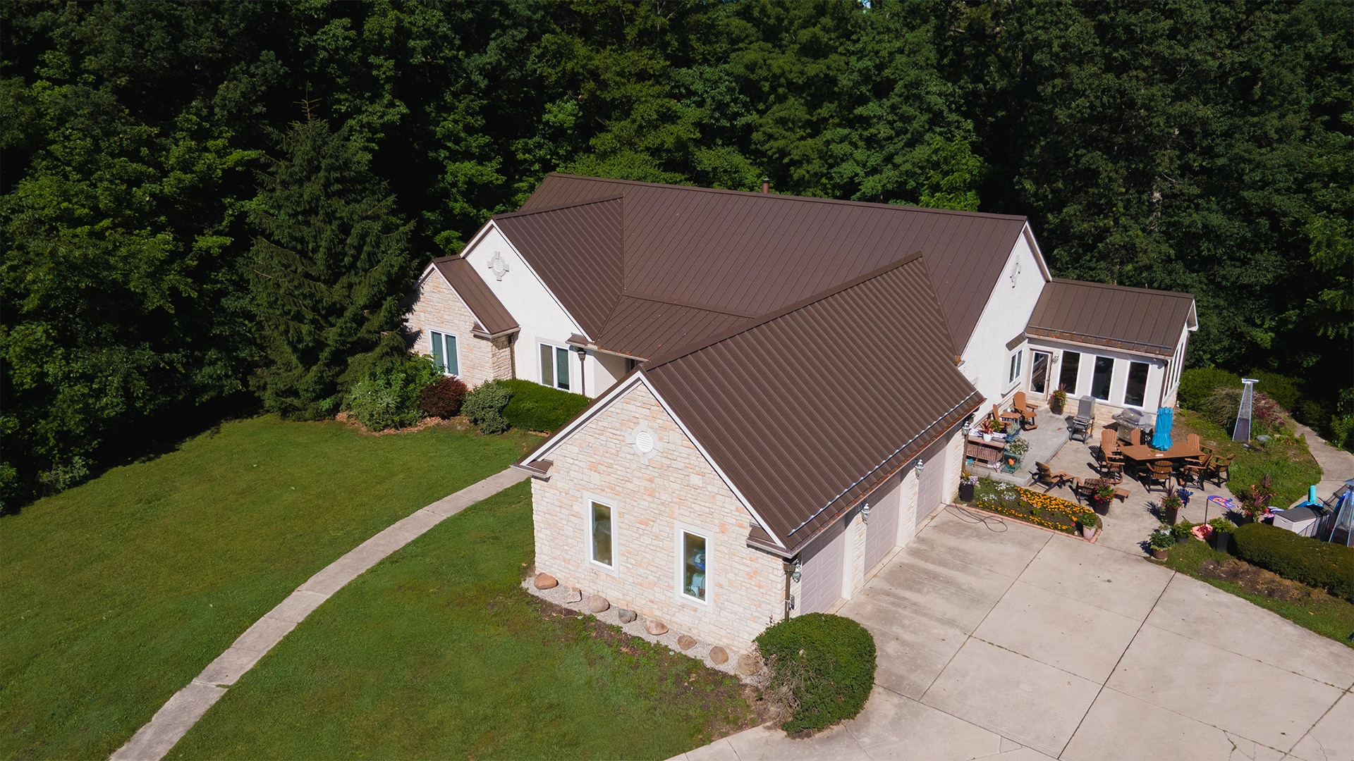 Aerial view of a stone and stucco home with a dark brown standing seam metal roof and multiple gables.
