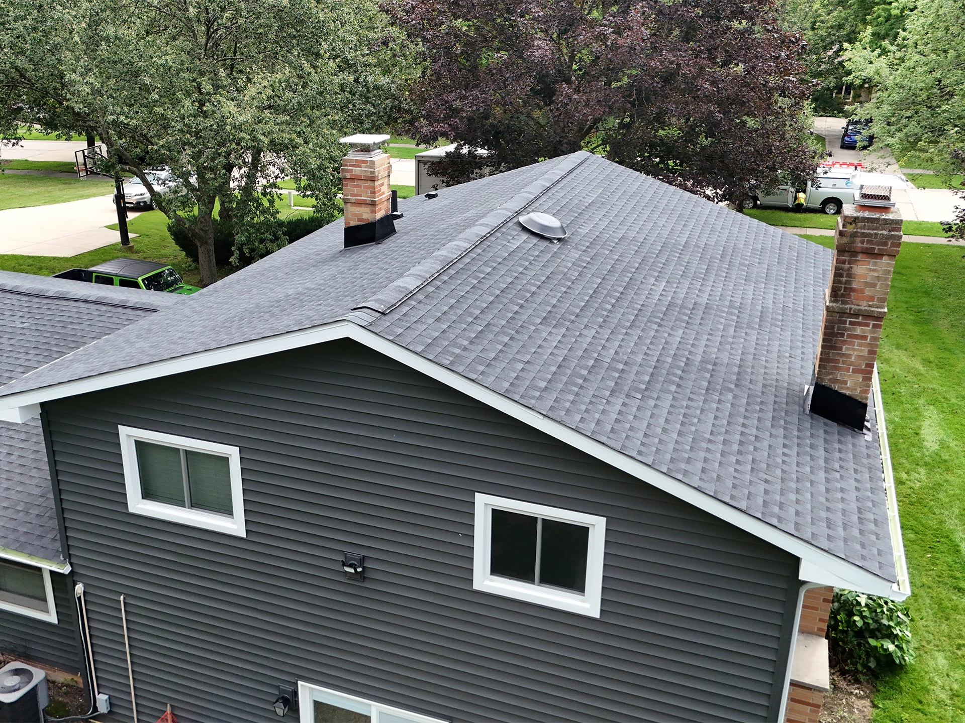 Aerial view of a finished gray shingle roof and matching charcoal siding with white trim on a two-story home.