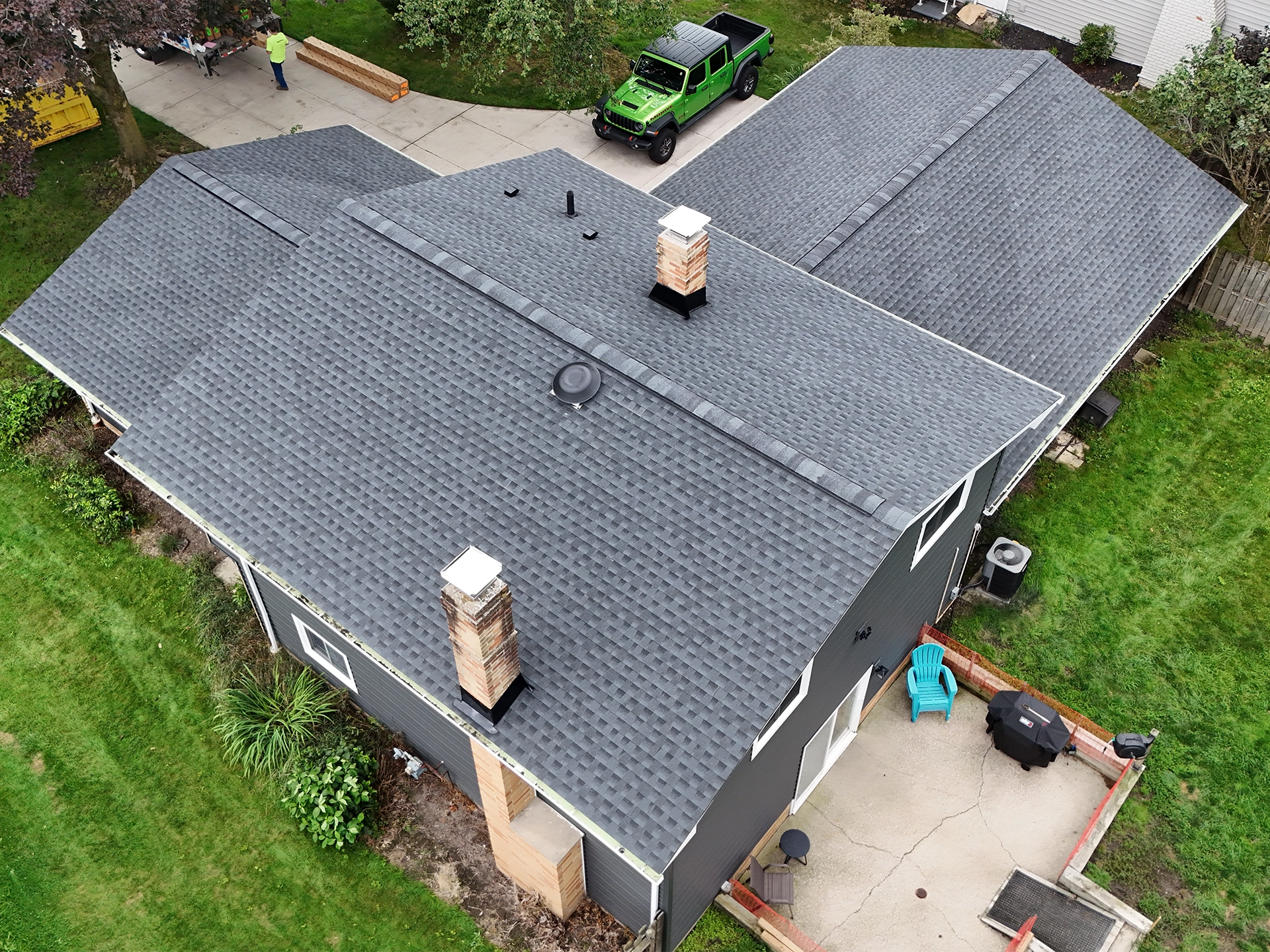 Overhead drone view of a completed gray architectural shingle roof on a ranch home with two brick chimneys and a roof vent.