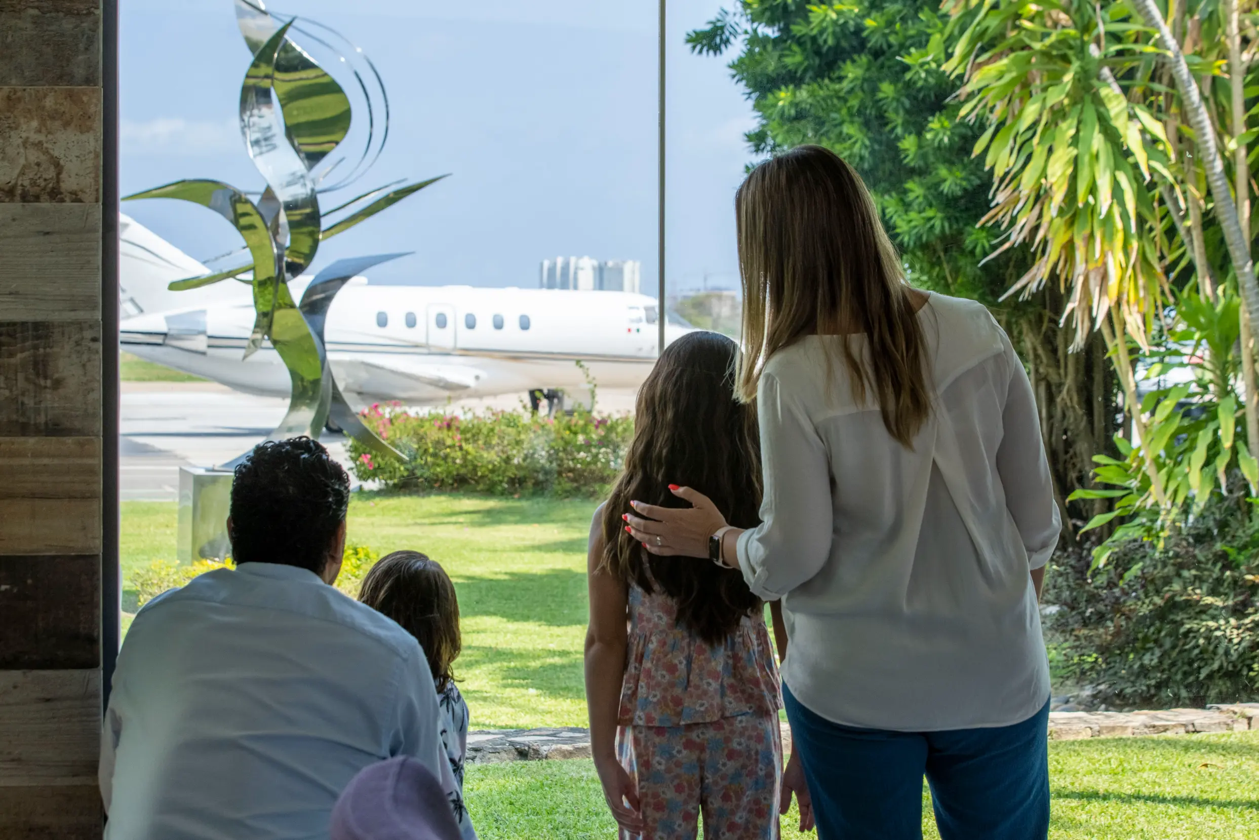 Family of four looking out at a private jet parked on an airstrip through a large window.