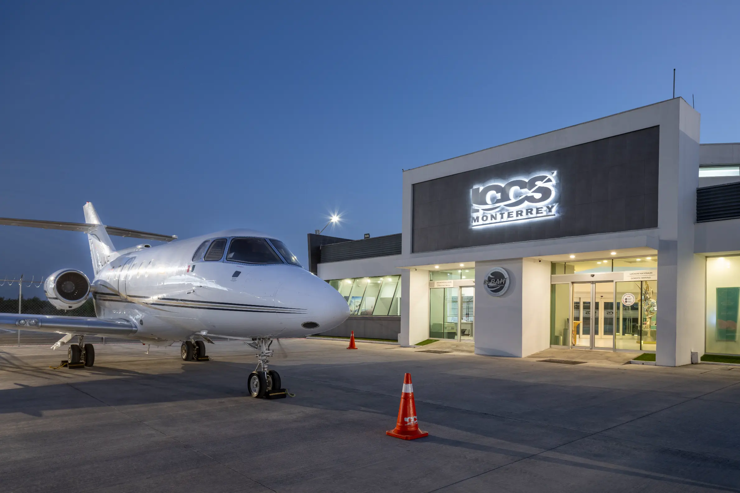 Private jet parked in front of the ICCS Monterrey building at dusk with clear sky.