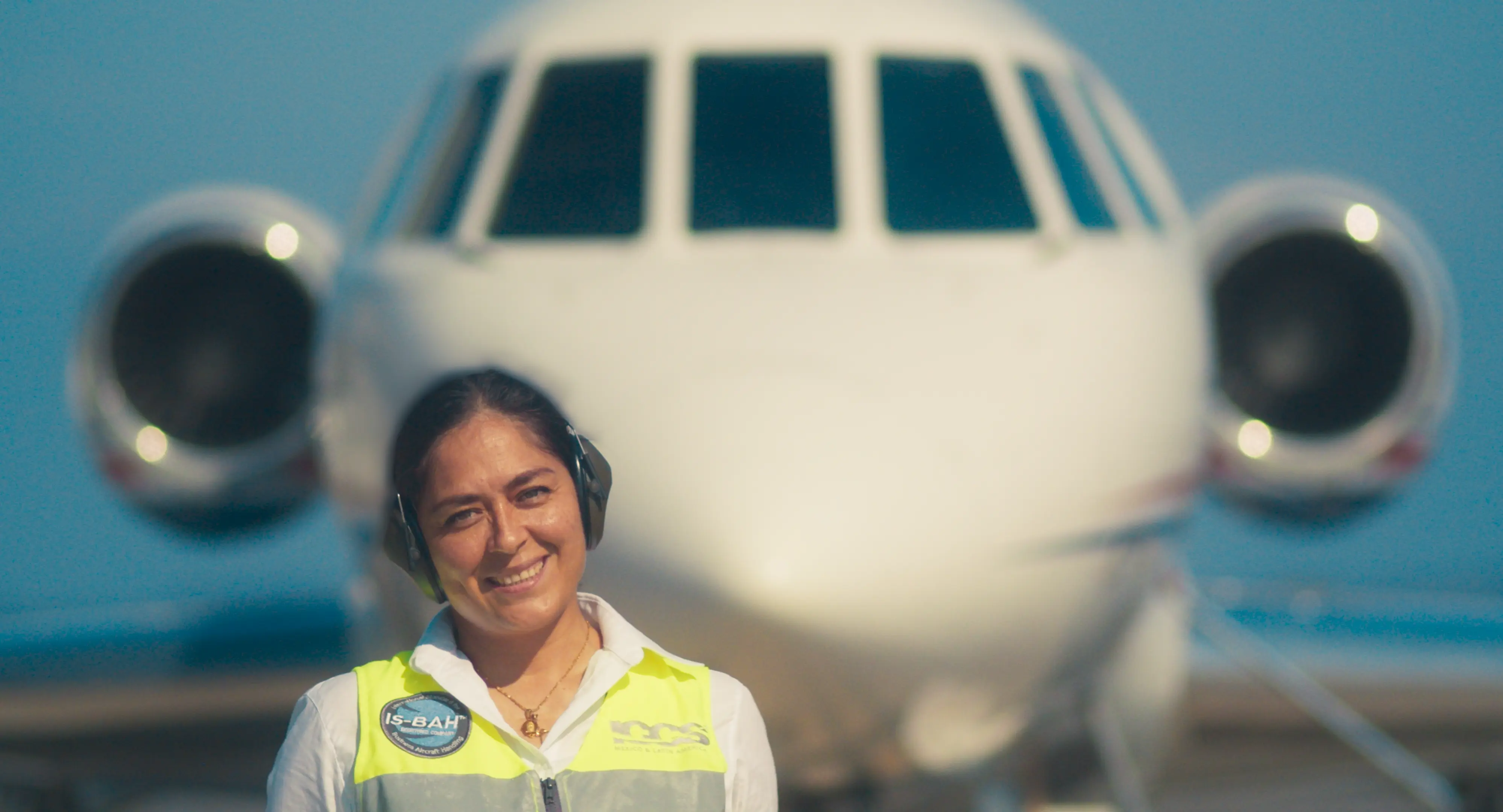 Smiling female airport ground crew member wearing headset and safety vest standing in front of a white jet airplane.