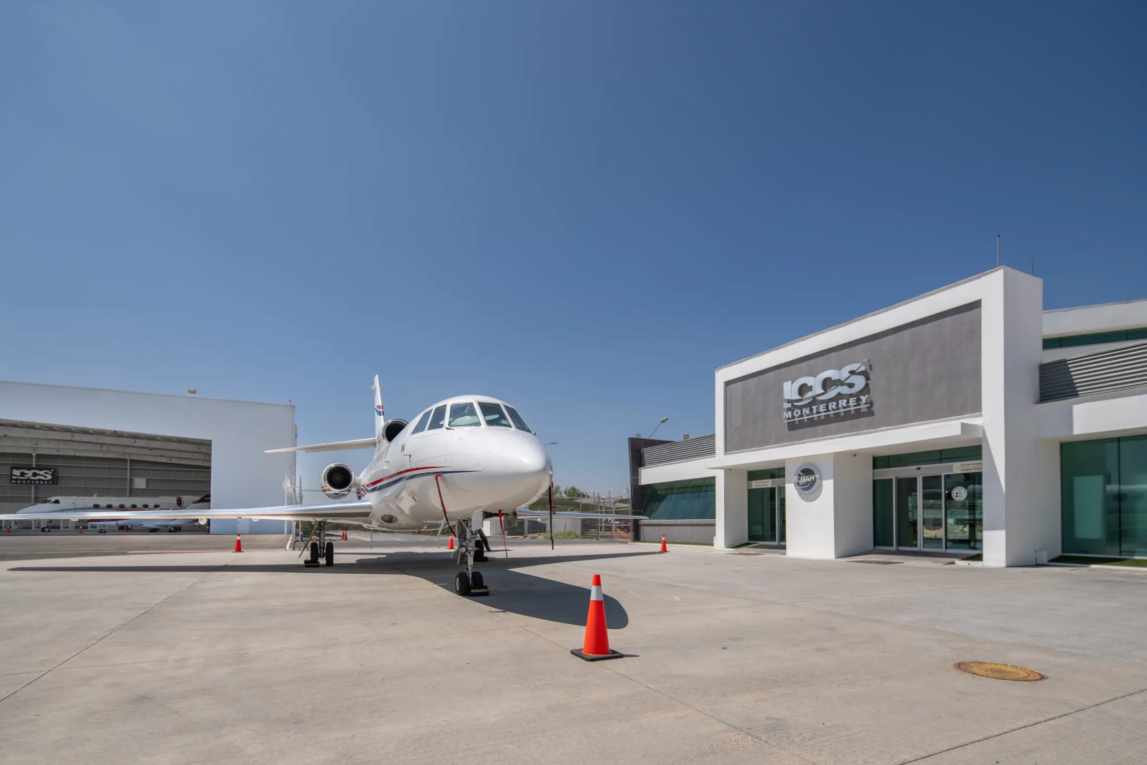 White private jet parked on a concrete tarmac in front of a modern building with ICCS Monterrey signage under a clear blue sky.