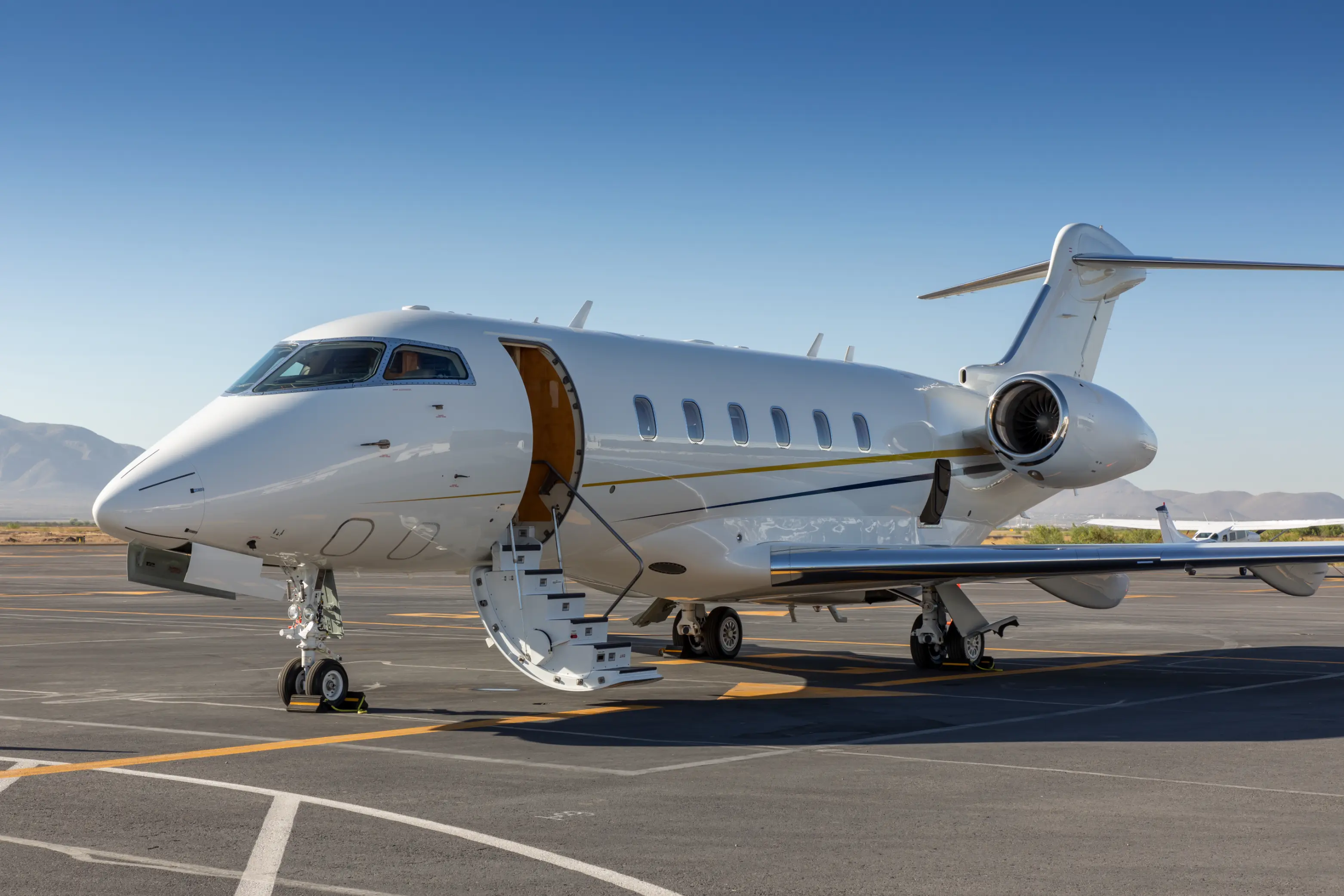 White private jet parked on an airport tarmac with stairs extended and clear blue sky.