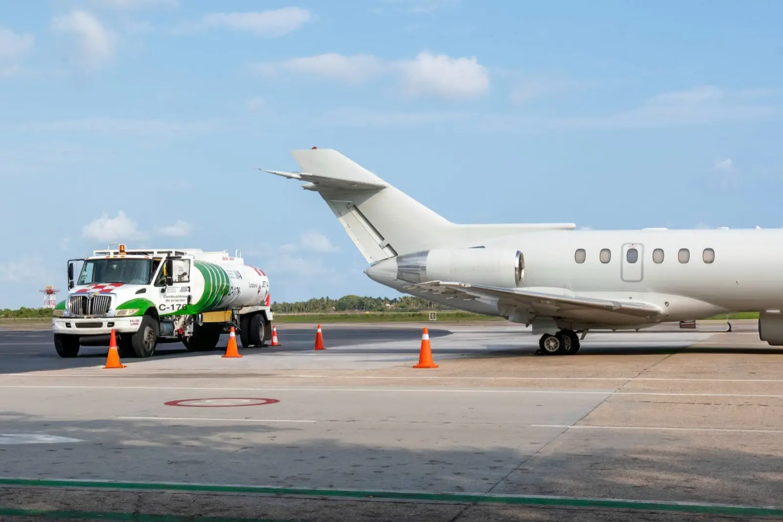 Fuel tanker truck parked on tarmac near the tail of a white private jet under a partly cloudy sky.
