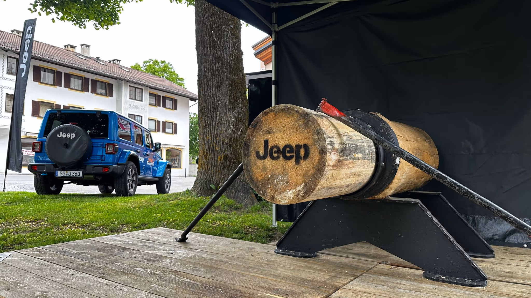 Ein blauer Jeep steht neben einem dicken Holzstamm, der ebenfalls mit Jeep gebrandet ist.