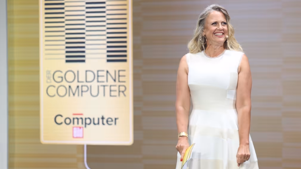 Eine Frau im weißen Kleid steht neben einem Banner des goldenen Computers.