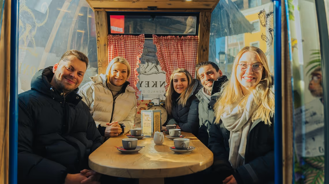Fünf Personen sitzen in einem kleinen Zelt und trinken Kaffee.