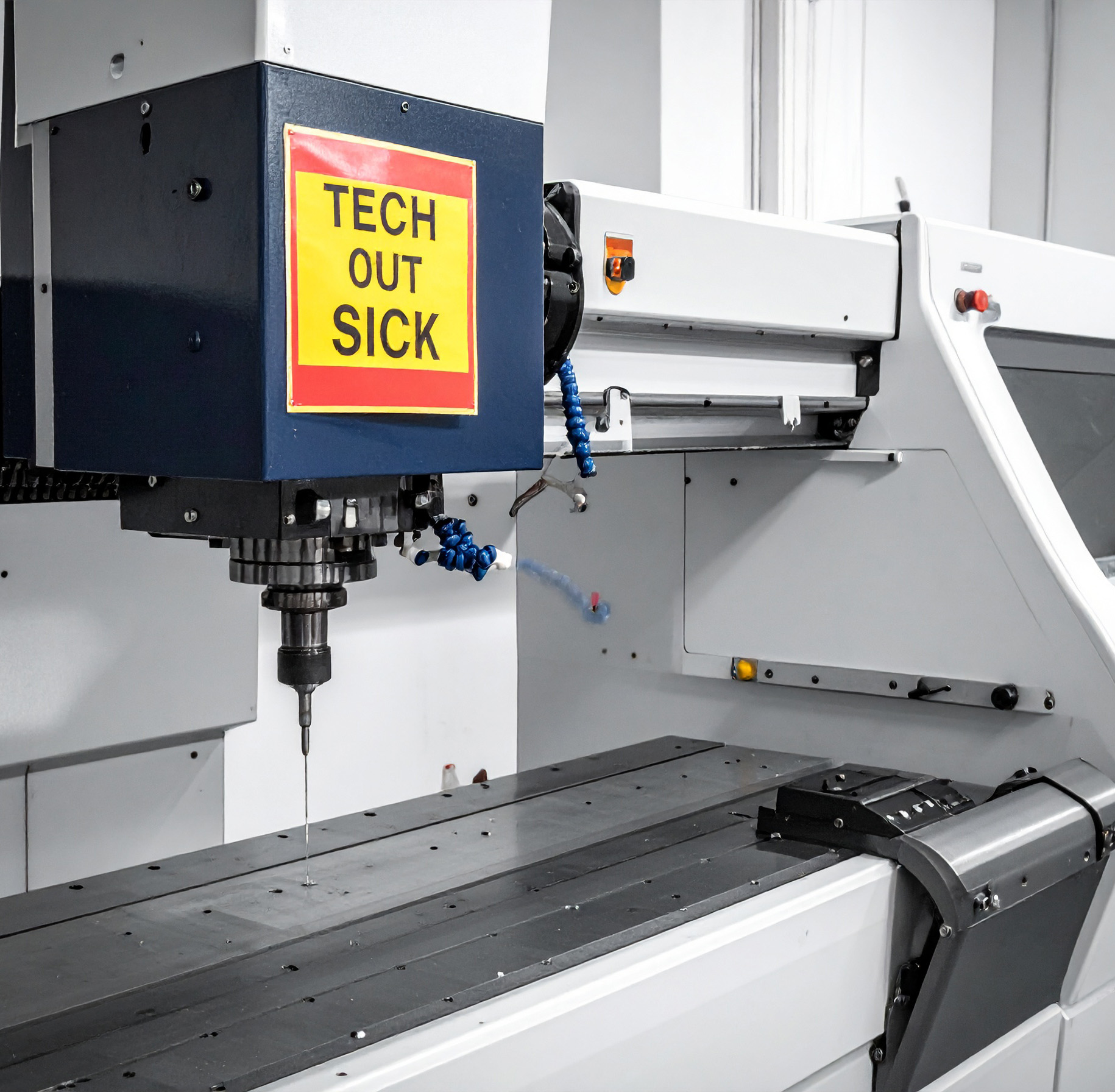 A CNC machine sitting idle with a red and yellow sign taped to it saying "Tech Out Sick"