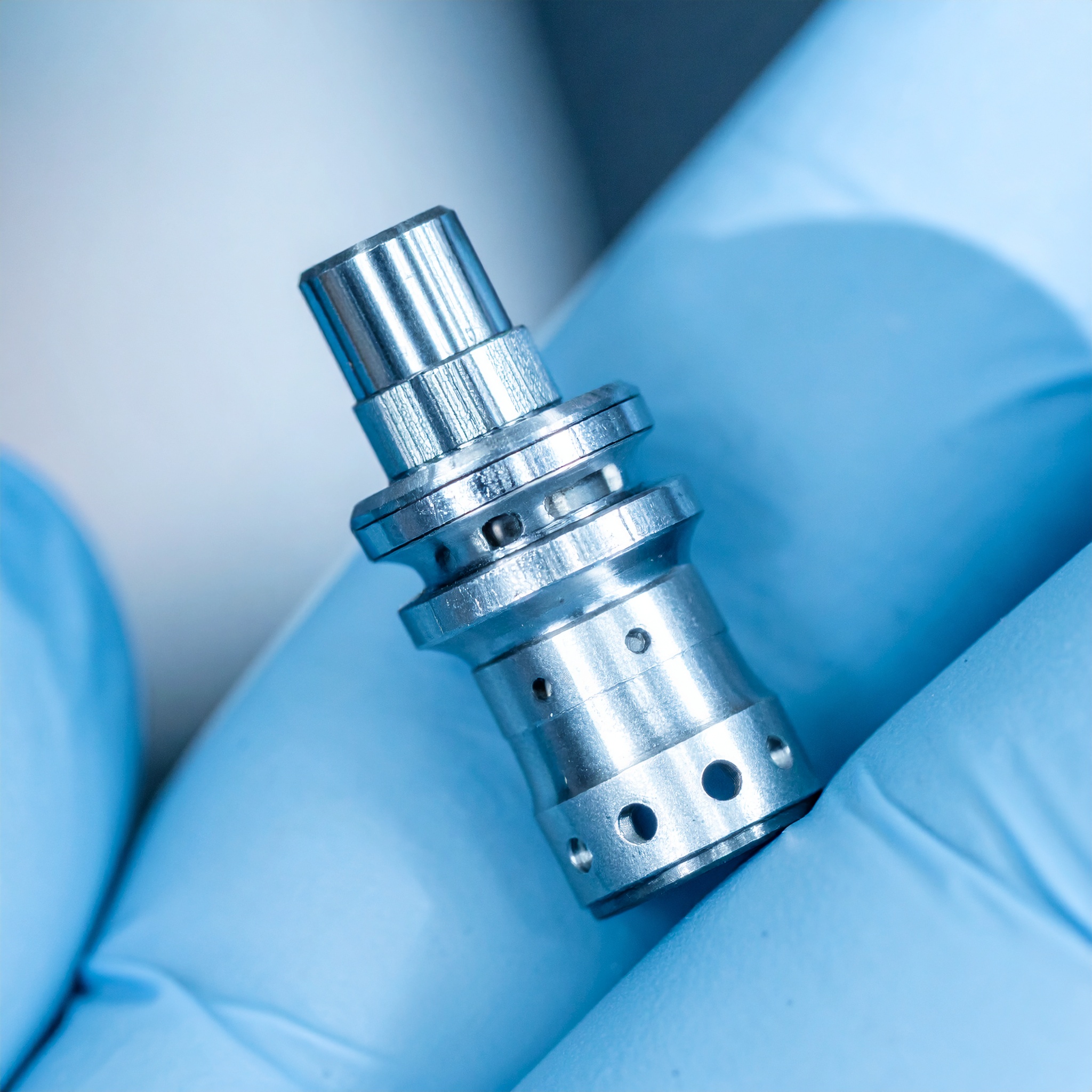 Gloved hand holding a tiny  complex machined part