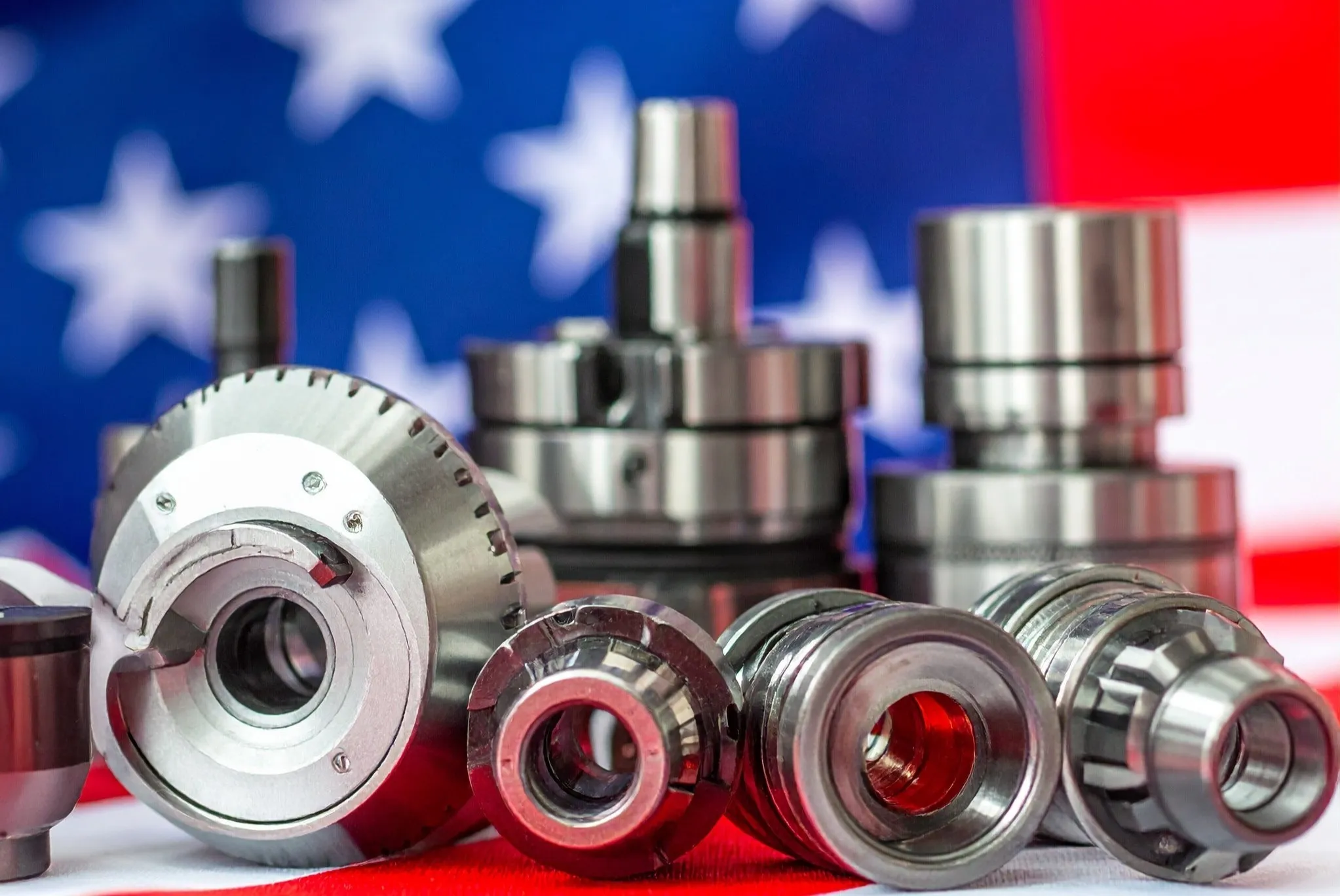 Close-up of metal machinery parts arranged on a surface with an American flag blurred in the background.