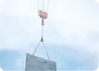 A concrete slab is suspended by a crane against a clear blue sky. The crane's red-and-white striped hook adds contrast, suggesting construction work.