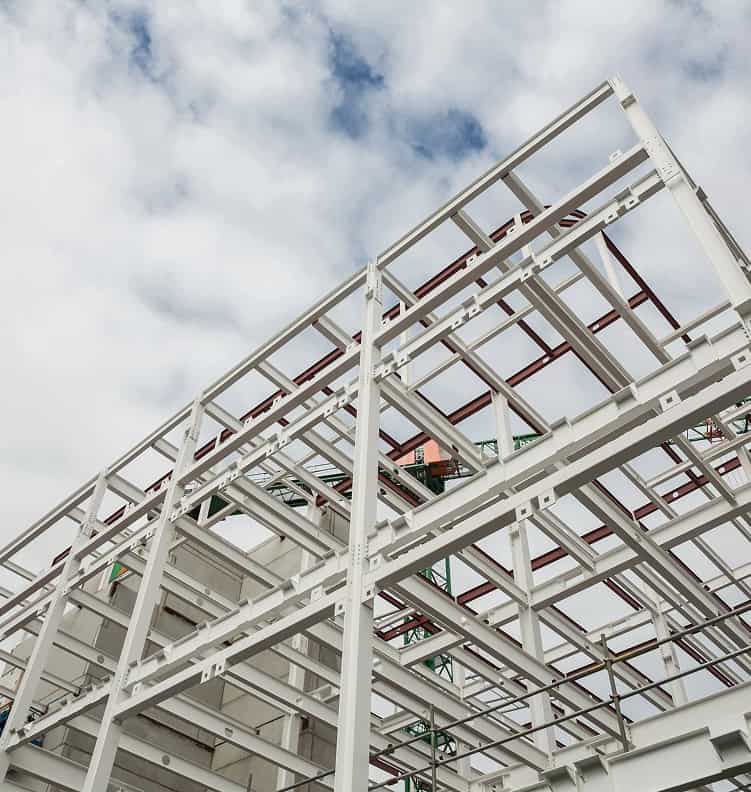 Steel framework of an unfinished building against a partly cloudy sky. The structure showcases grid-like beams, creating an open, industrial feel.