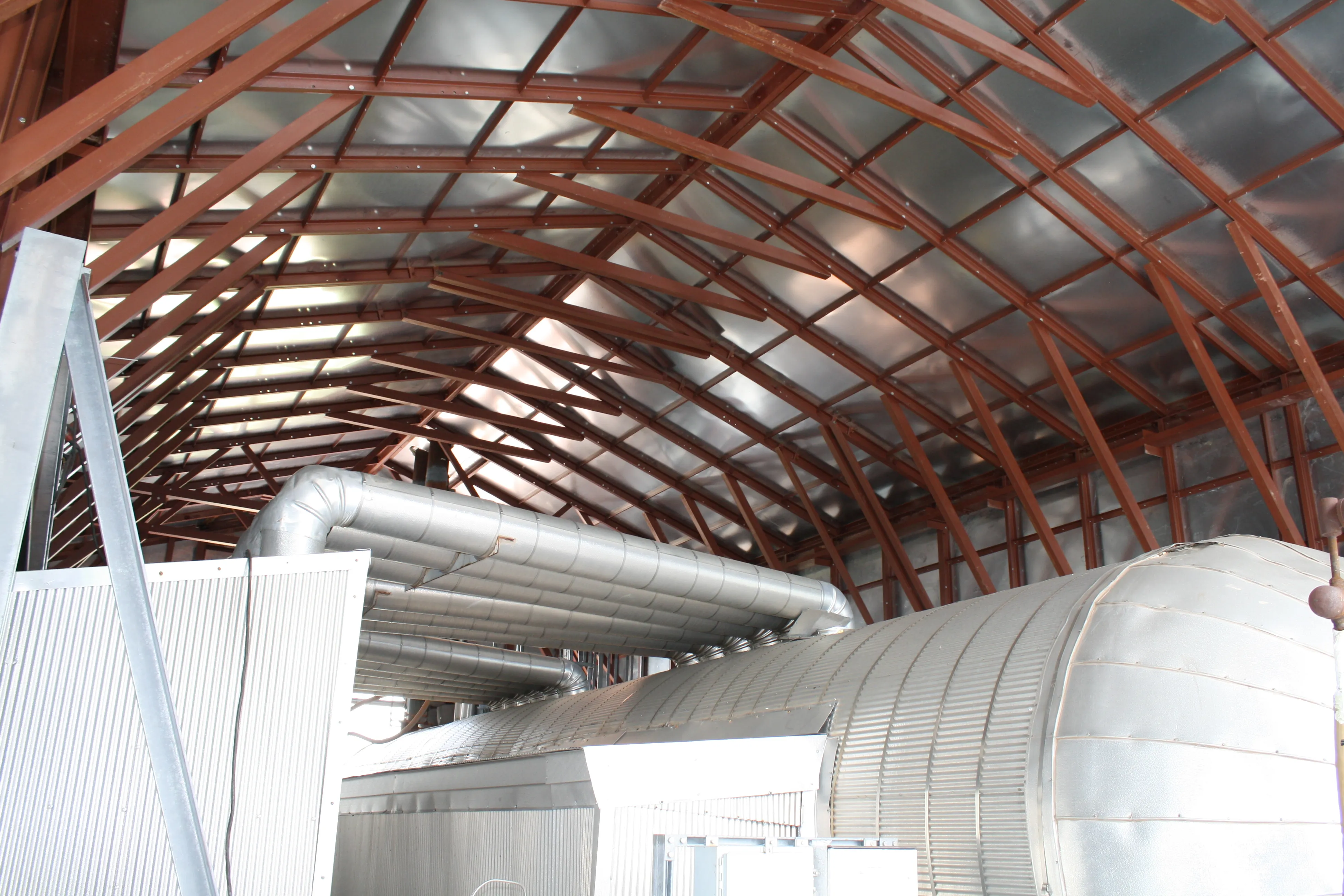 Interior of an industrial building showing curved red steel beams and large silver ventilation ducts.