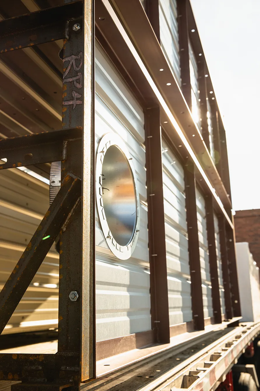 Close-up of metal industrial structure with a circular vent on a trailer, illuminated by sunlight.