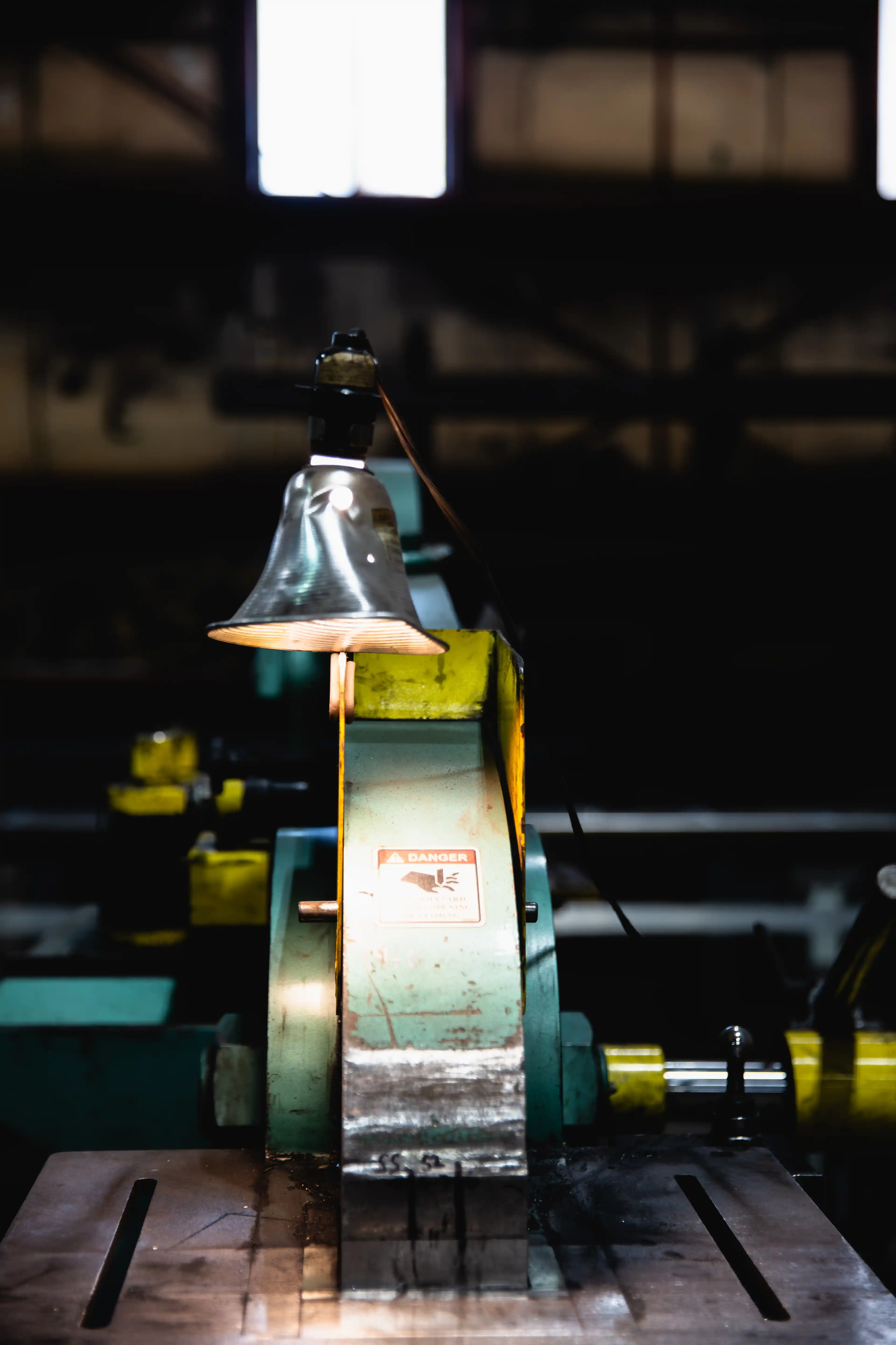 Industrial machine with a danger sign illuminated by a hanging metal lamp in a dark workshop.