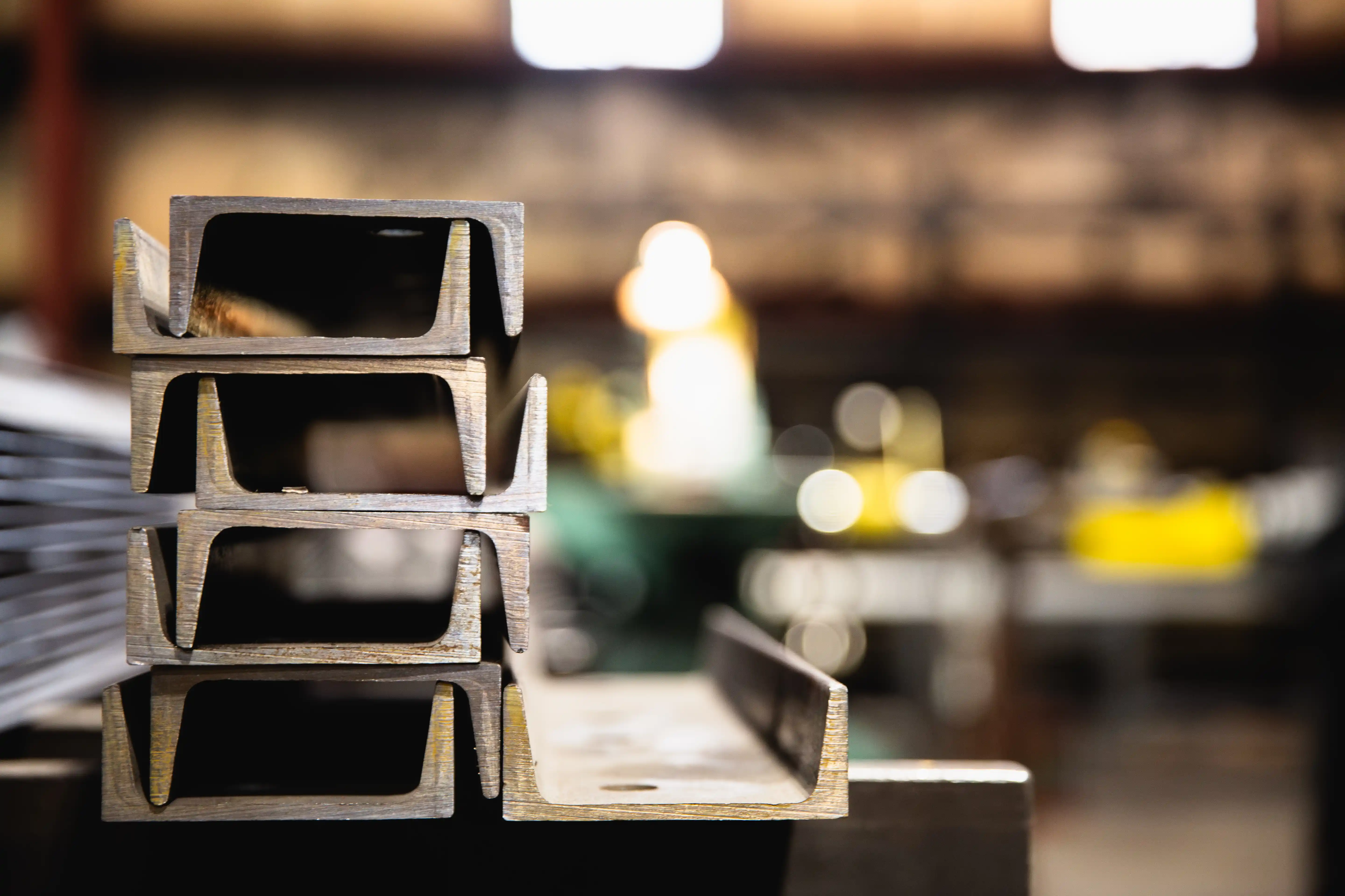 Stacked industrial metal beams with a blurred workshop background.