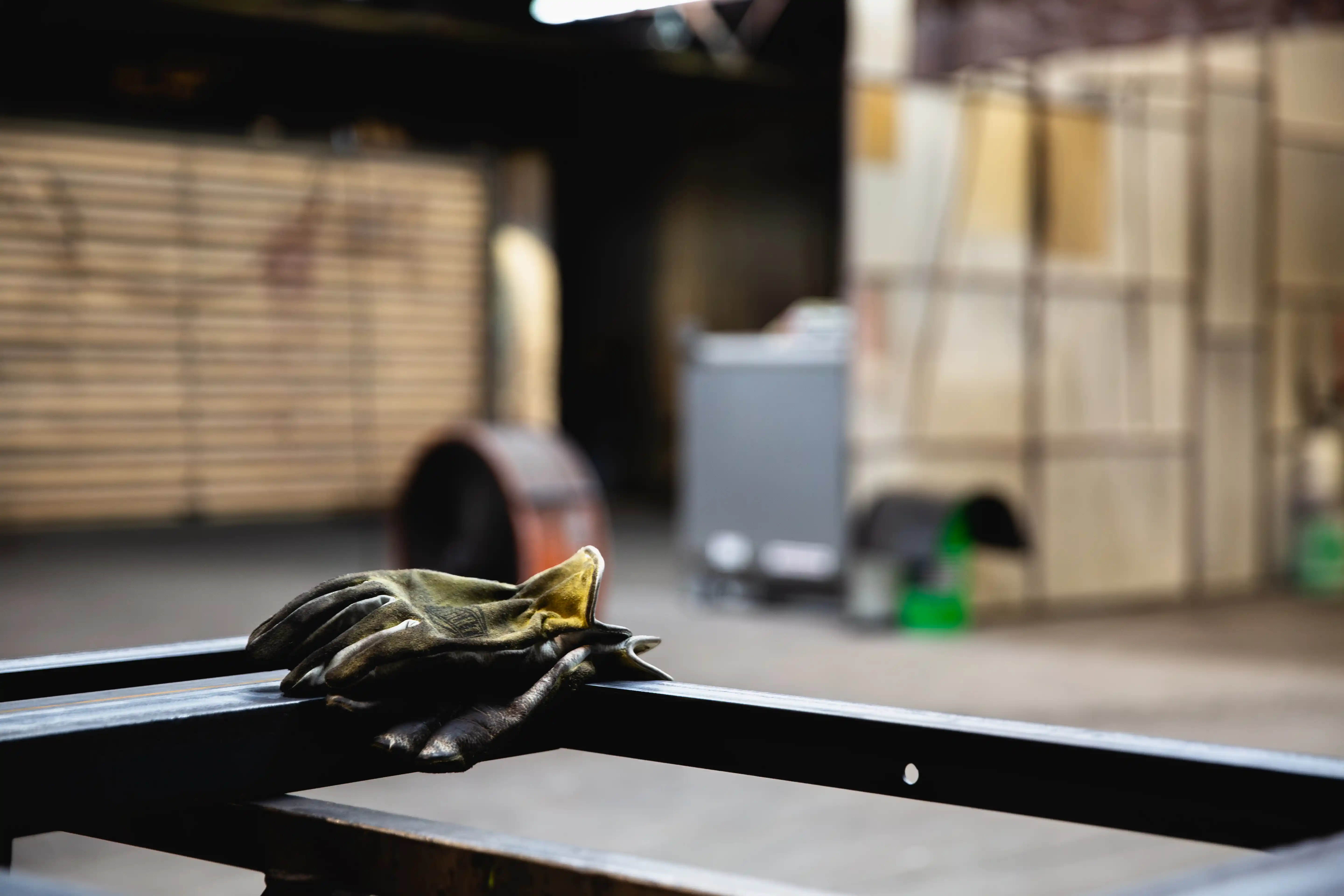 A worn pair of work gloves resting on a metal frame in an industrial workshop setting.