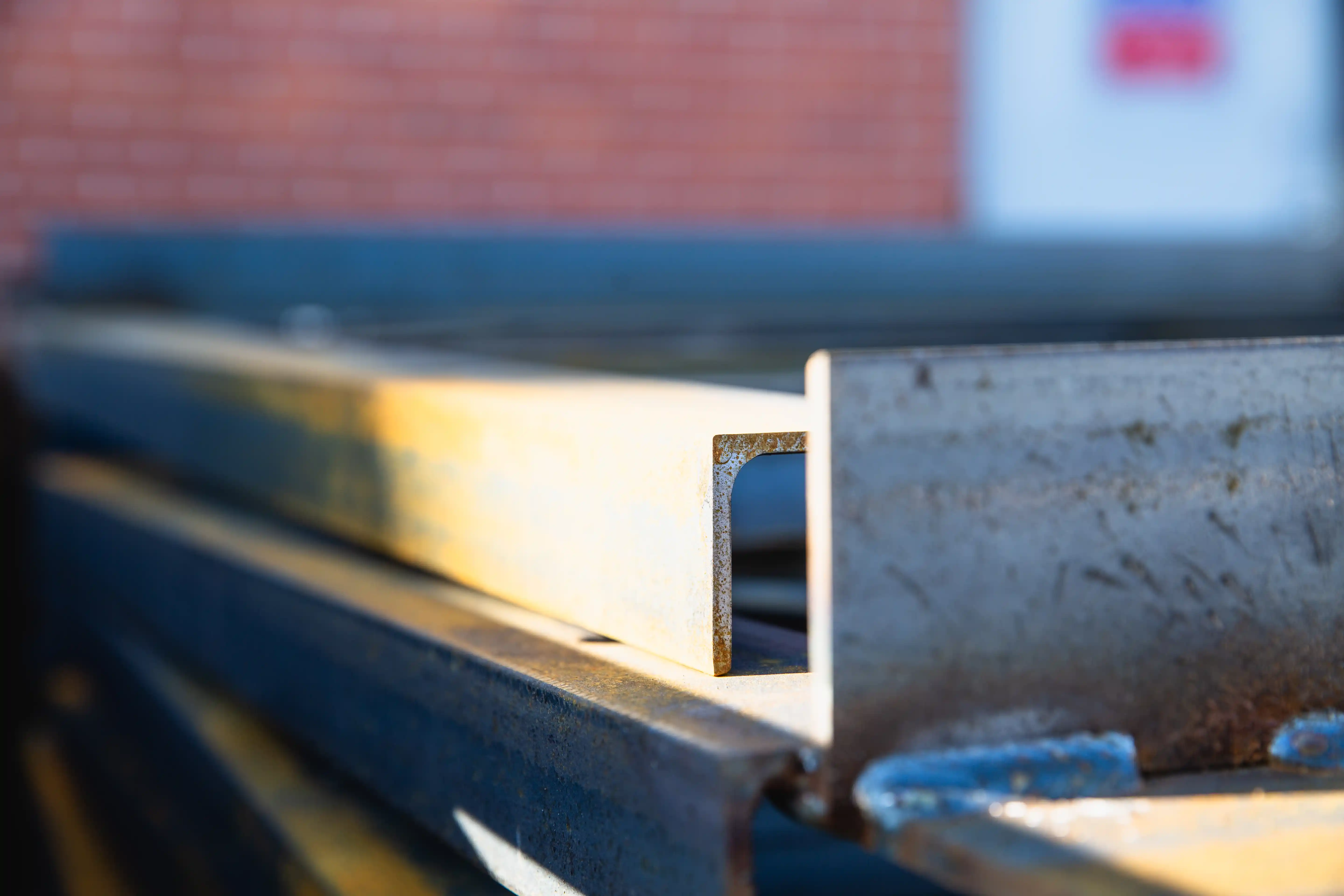 Close-up of a rusted steel beam with a blurred brick wall in the background.