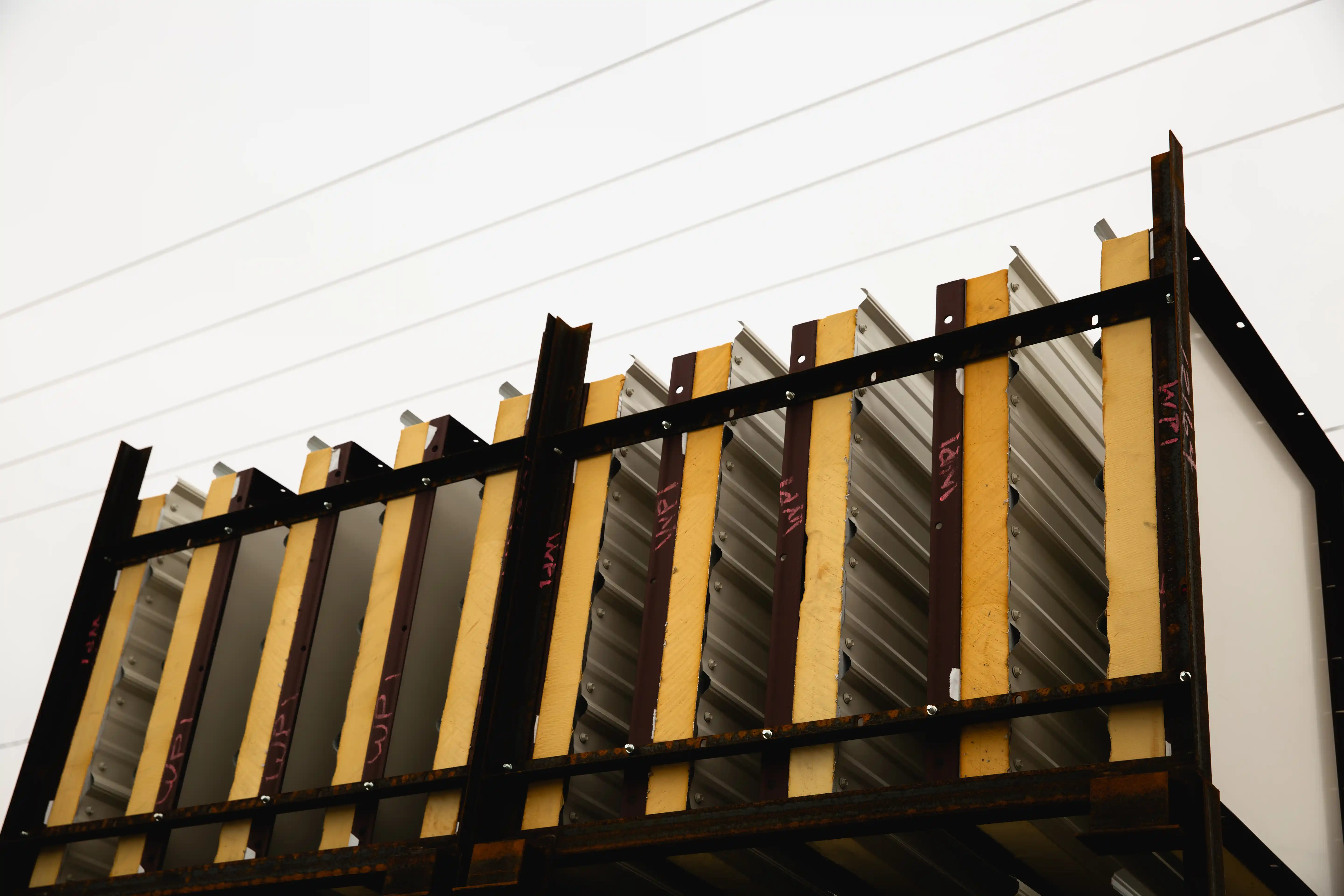 Metal and wooden structure with diagonal corrugated panels against a pale sky.