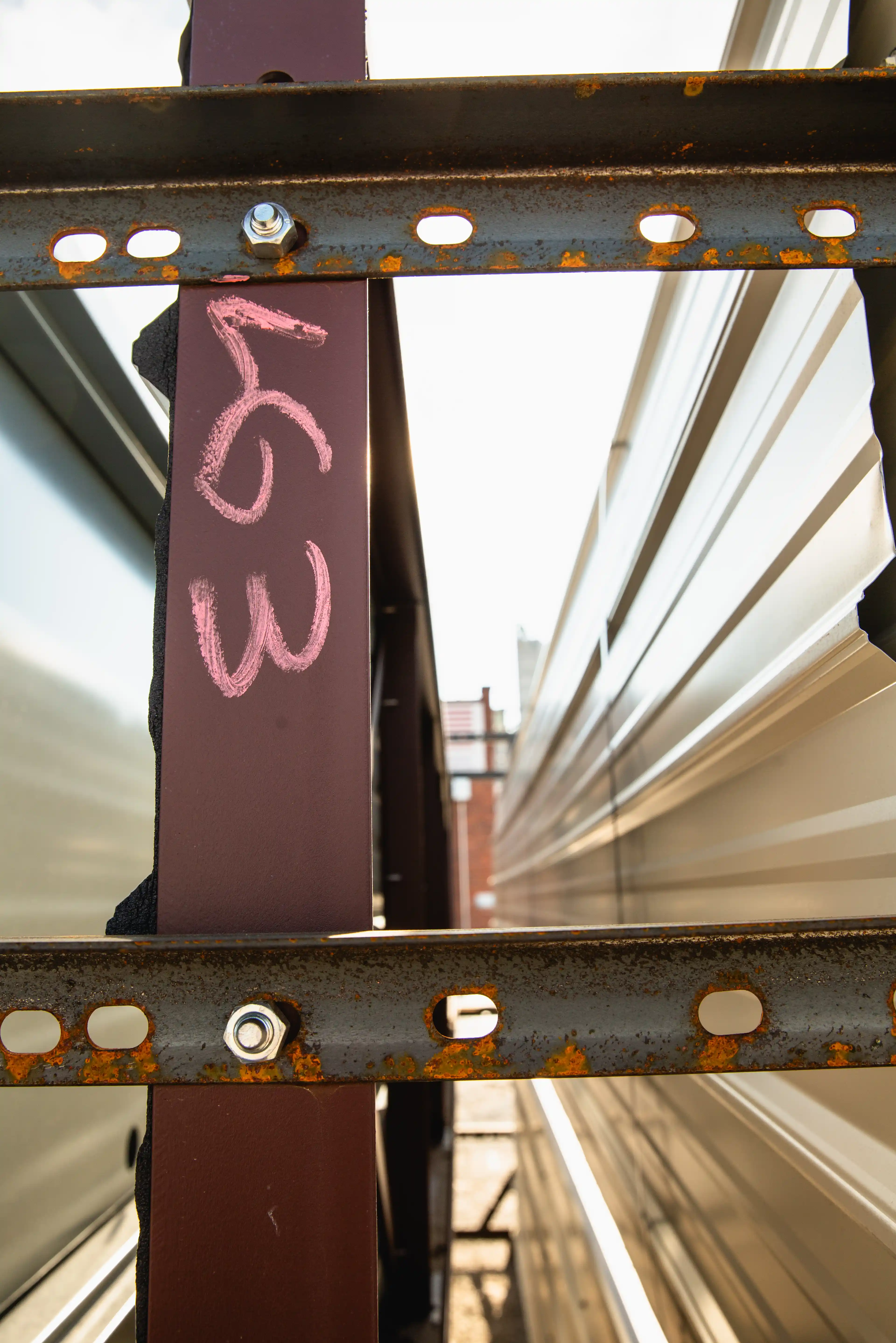 Rusty metal frame with bolts beside a maroon support beam marked 163 in pink chalk.