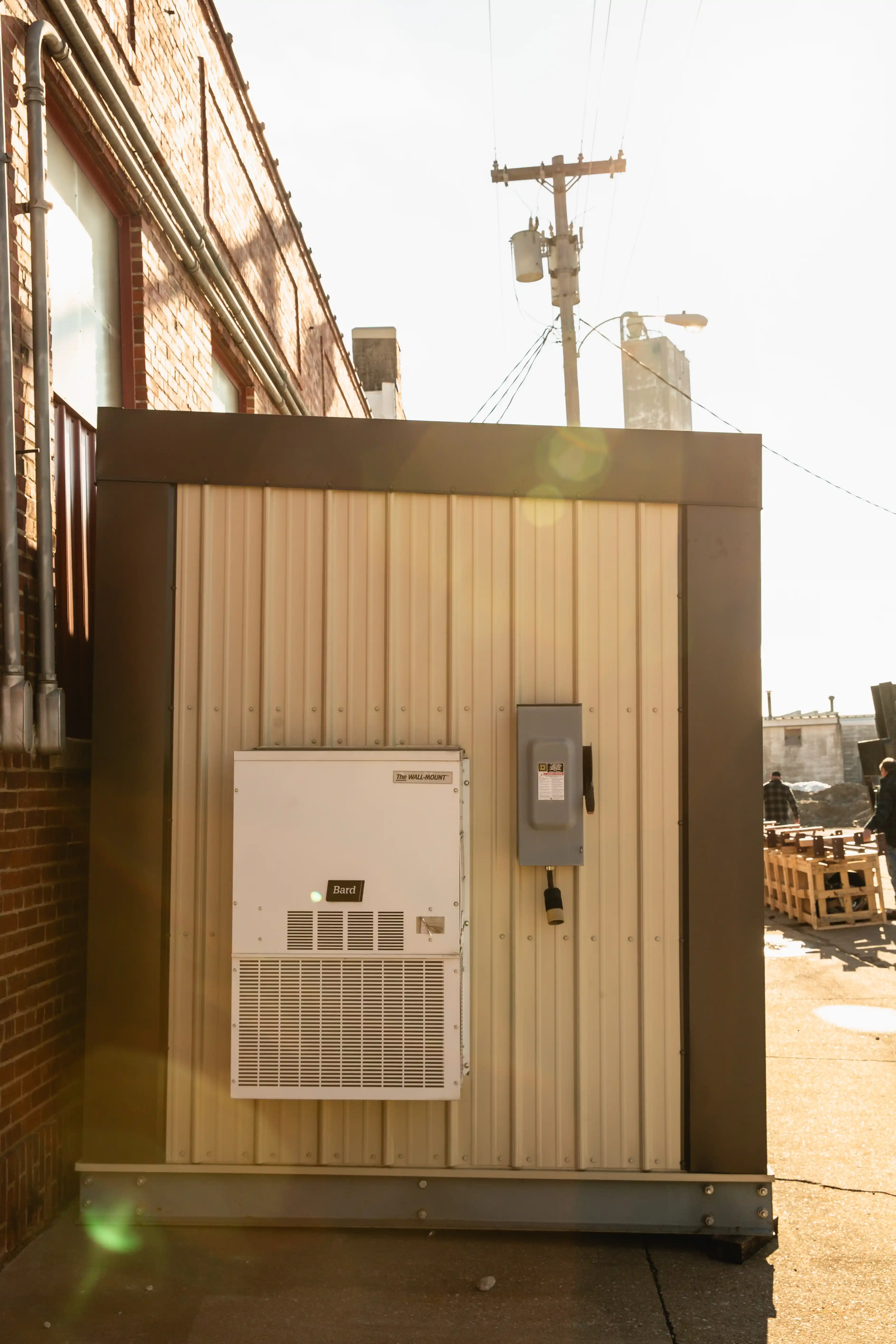 Wall-mounted white Bard air conditioning unit on a beige metal wall outdoors in bright sunlight.