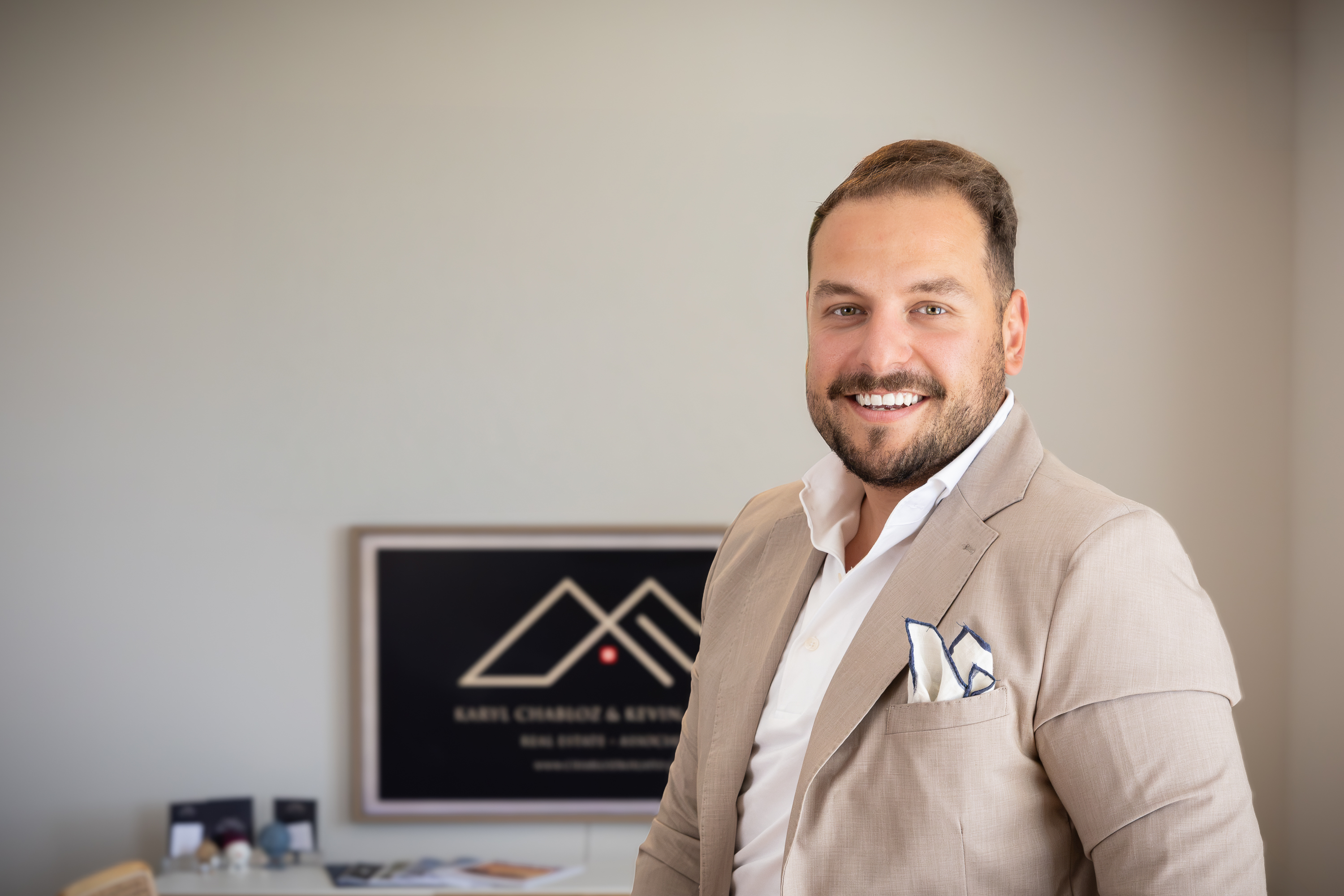 Deux personnes souriantes dans un bureau avec une table, chaises et photos de voiture de course et logo immobilier.