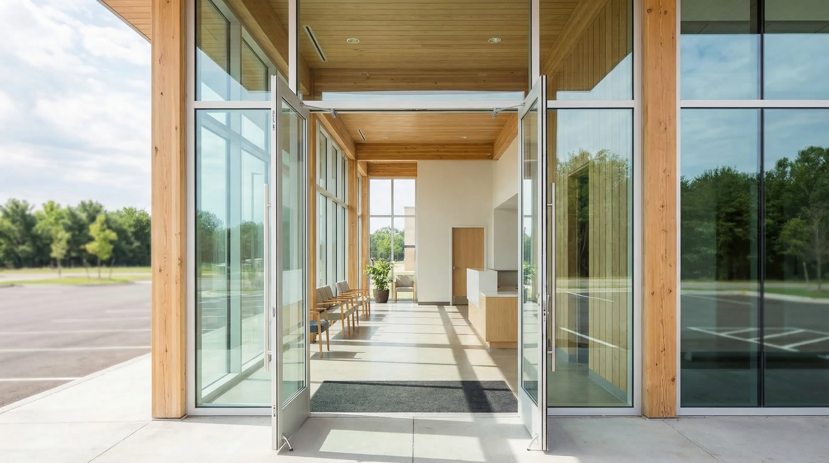Professional urgent care clinic entrance in Tulsa, OK — modern glass-front facility with Oklahoma blue sky and suburban parking lot