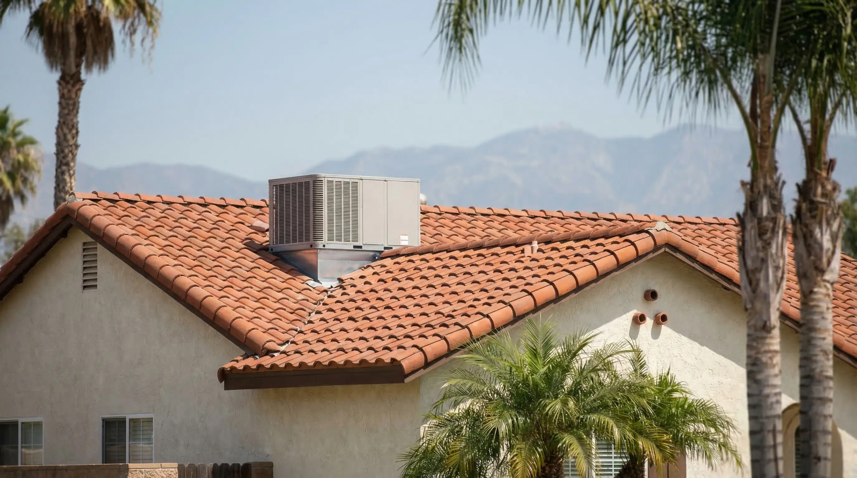 HVAC technician in uniform installing a rooftop air conditioning unit on a Spanish-style single-story home in the San Fernando Valley, Los Angeles, CA