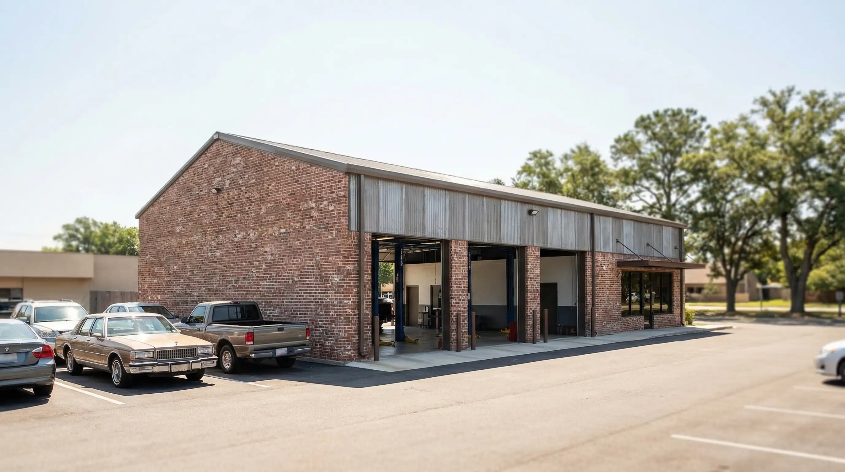 Independent auto repair shop exterior in a Montgomery, AL commercial strip with open service bays and vehicles in lot, bright Alabama sunshine