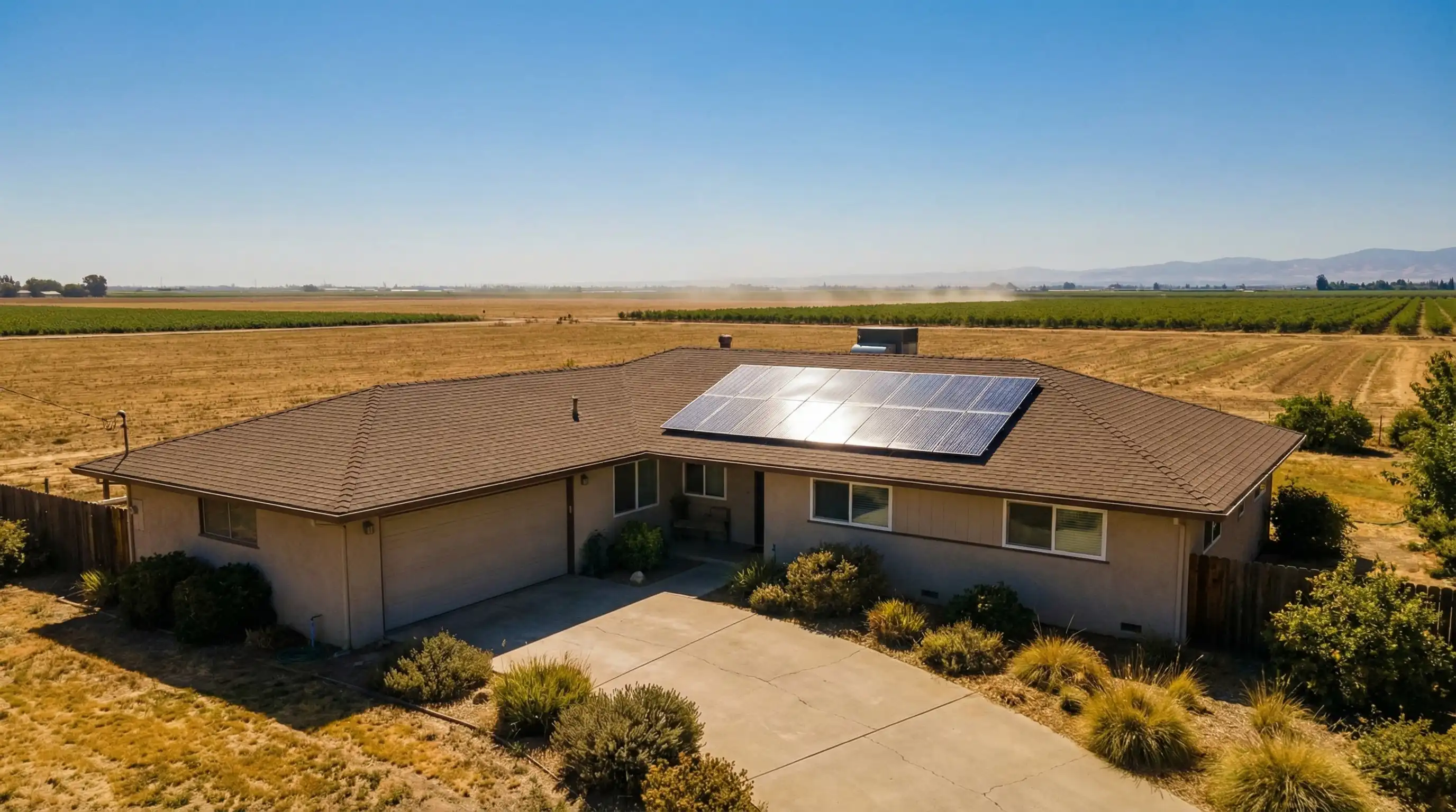 Aerial view of a Central Valley ranch home with solar panel array on roof, clear California sky, agricultural landscape in background, Stockton, CA