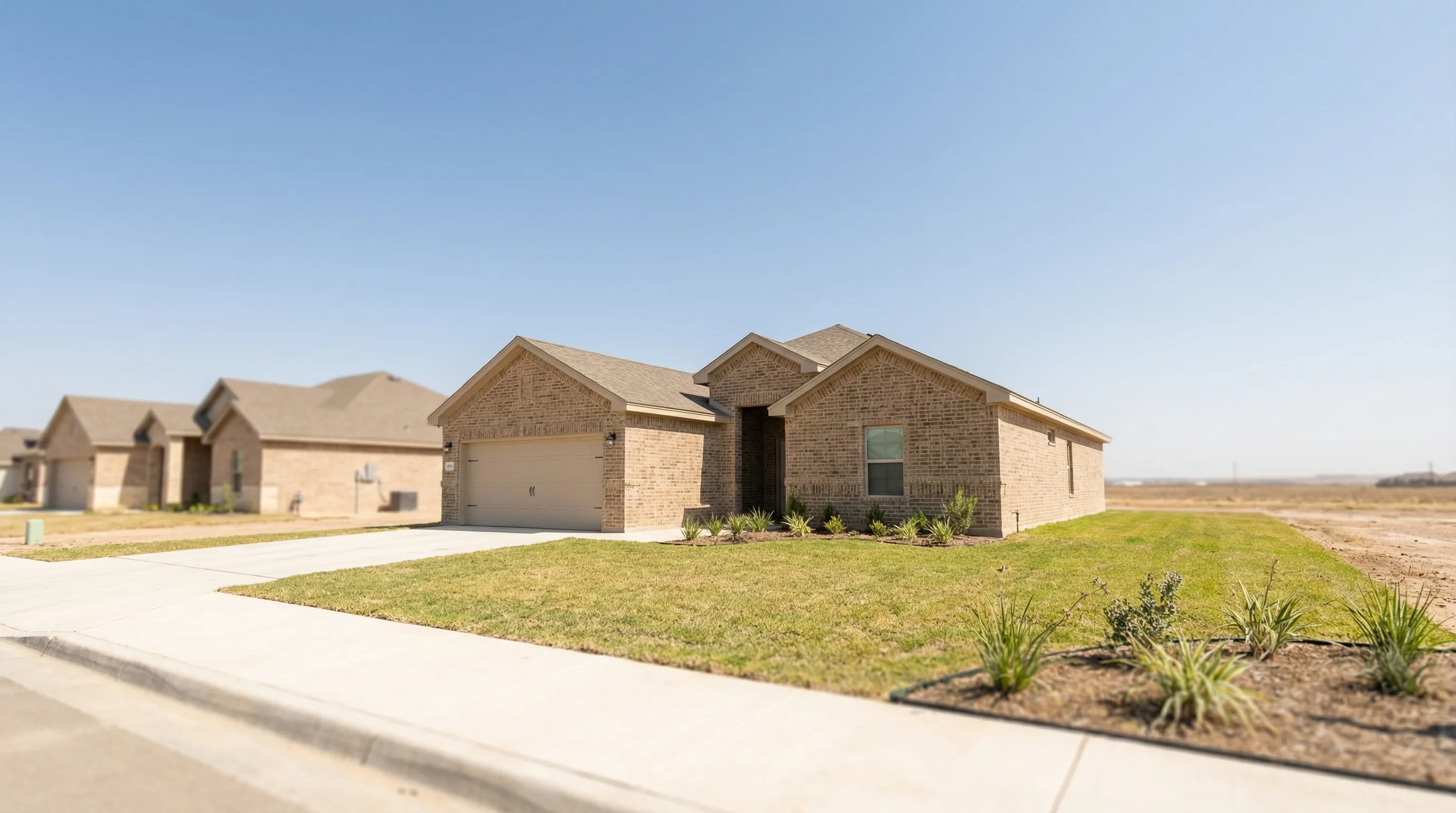 New construction single-family home exterior in NW Laredo TX Del Mar subdivision with for sale sign, tan brick facade, and South Texas blue sky
