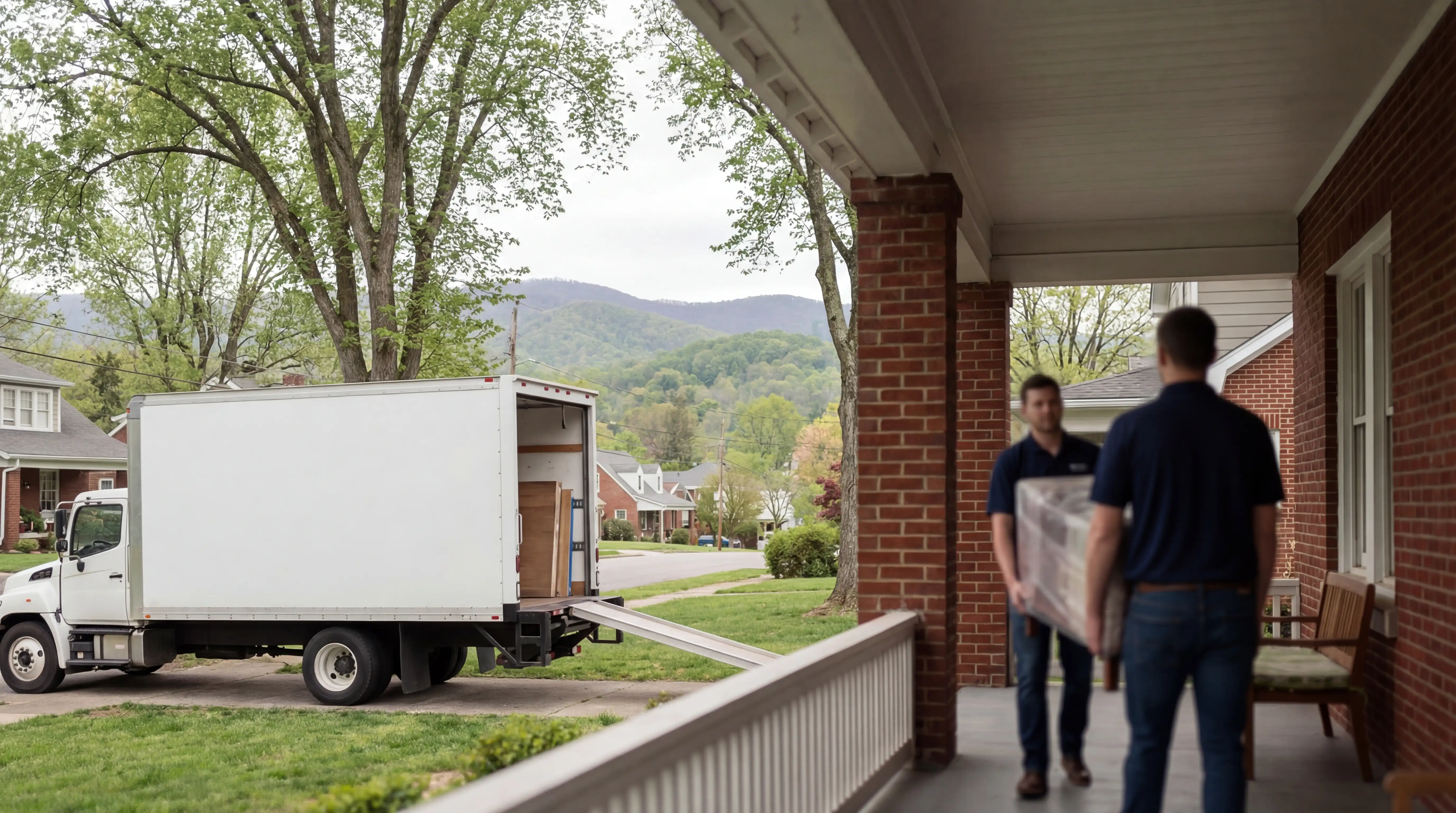 Moving truck parked in front of craftsman bungalow in Knoxville Fourth and Gill neighborhood, movers carrying furniture under Appalachian hardwood canopy, Tennessee spring morning