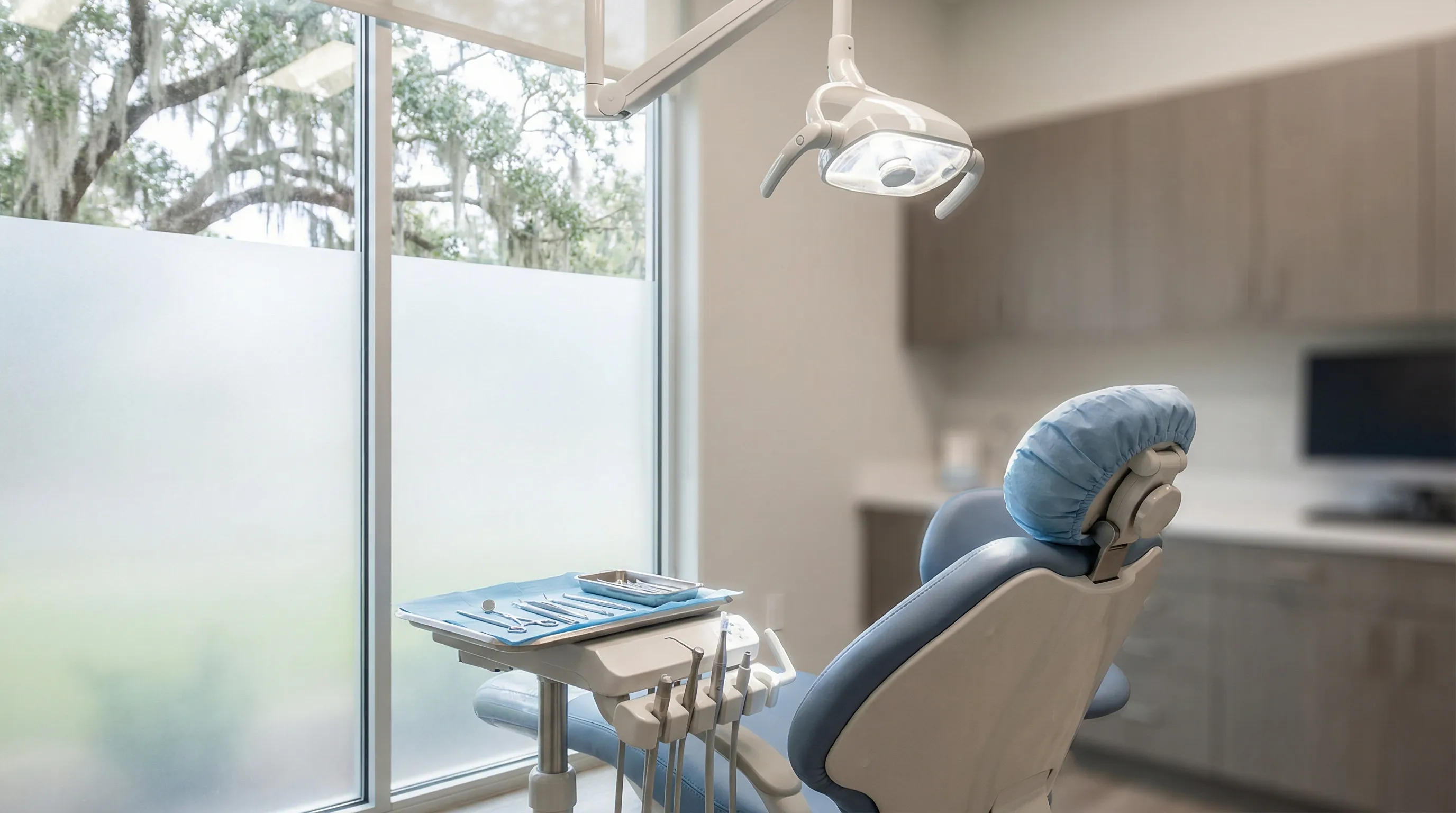 Modern Lafayette dental operatory with reclined patient chair, overhead clinical light, and sterilized instrument tray beside a south-facing window with soft Acadiana afternoon light
