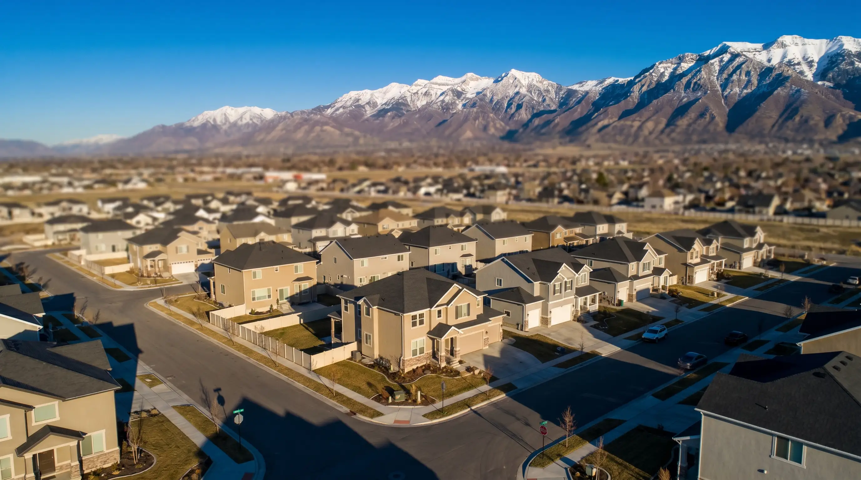 Real estate agent in business casual attire walking a young couple through the front door of a newly listed two-story home in Orem, UT, with Wasatch Mountains visible through the window in the background