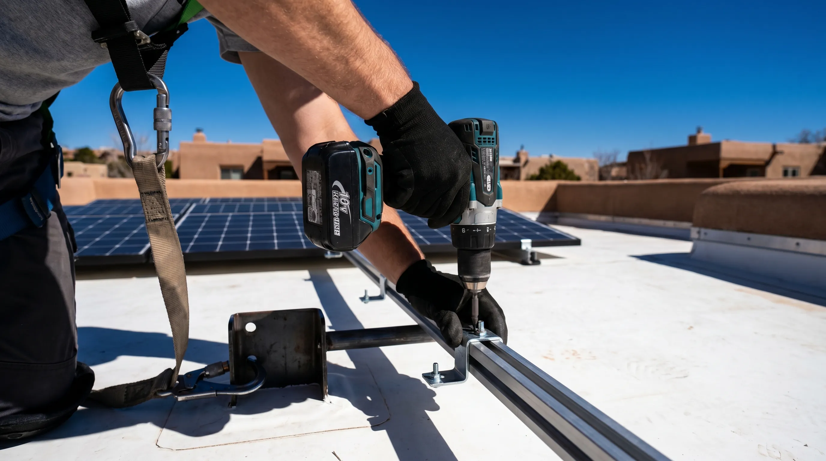 Solar installation technician mounting panel brackets on a Santa Fe adobe home's flat roof with safety harness, high-altitude desert sunlight illuminating completed panel rows in background