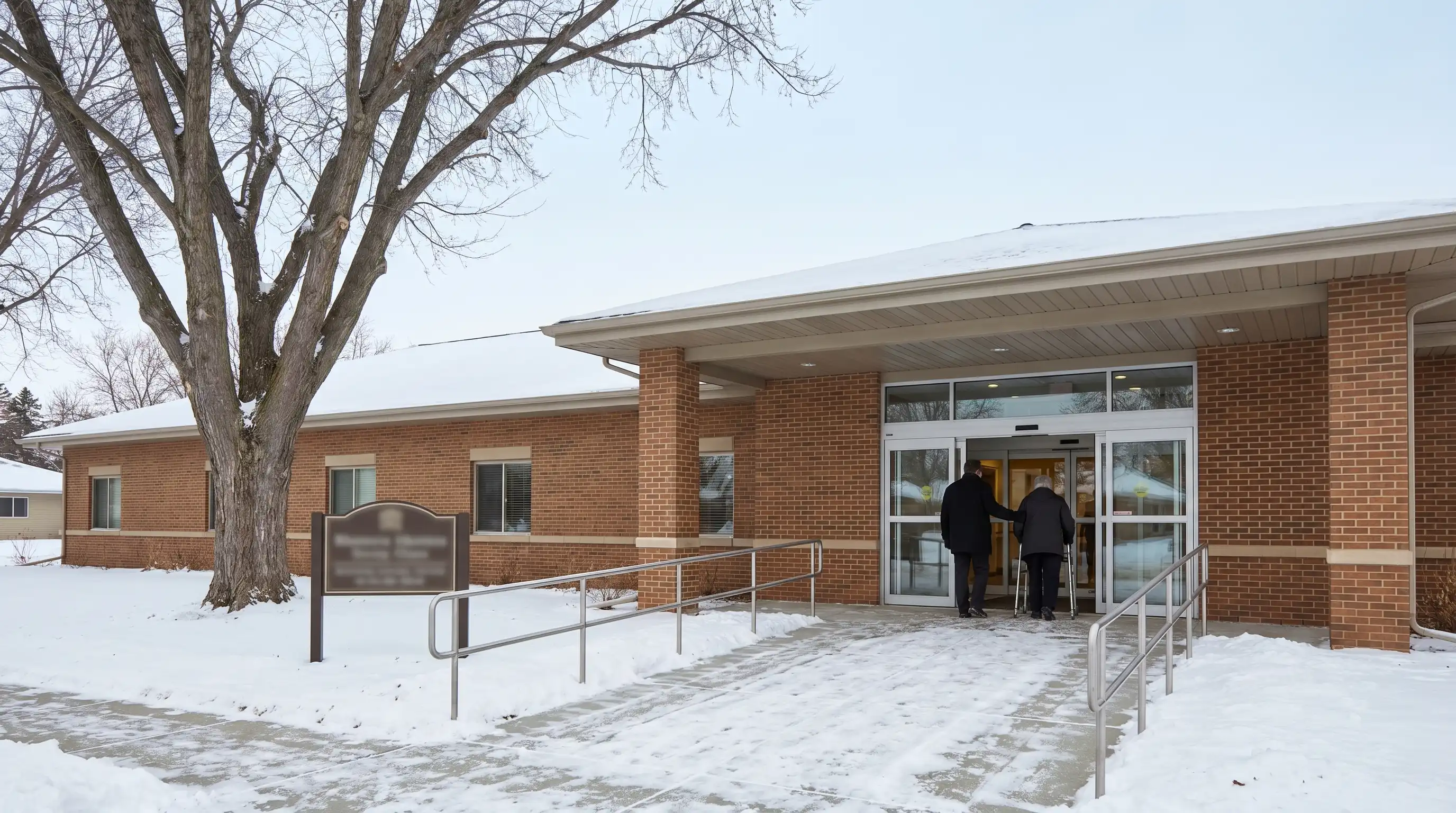 Caregiver in company-branded uniform assisting an elderly resident in a warmly lit Grand Forks, ND assisted living common area