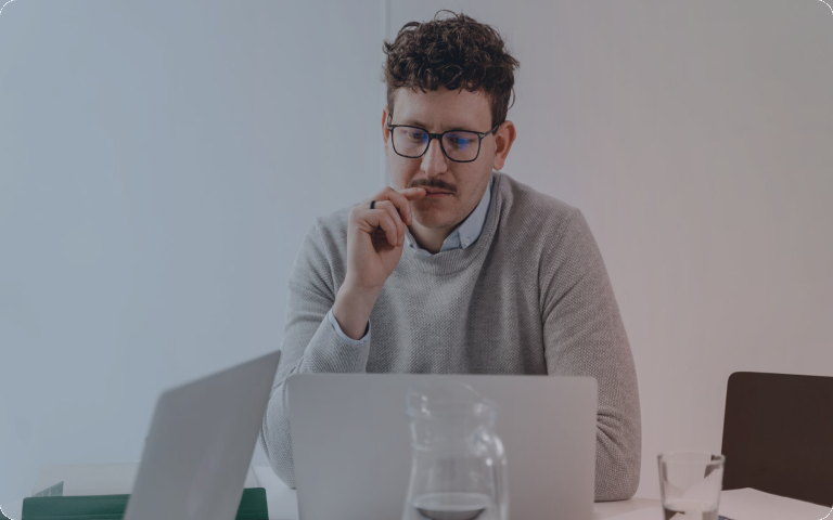 A man in glasses pausing to think in front of a laptop