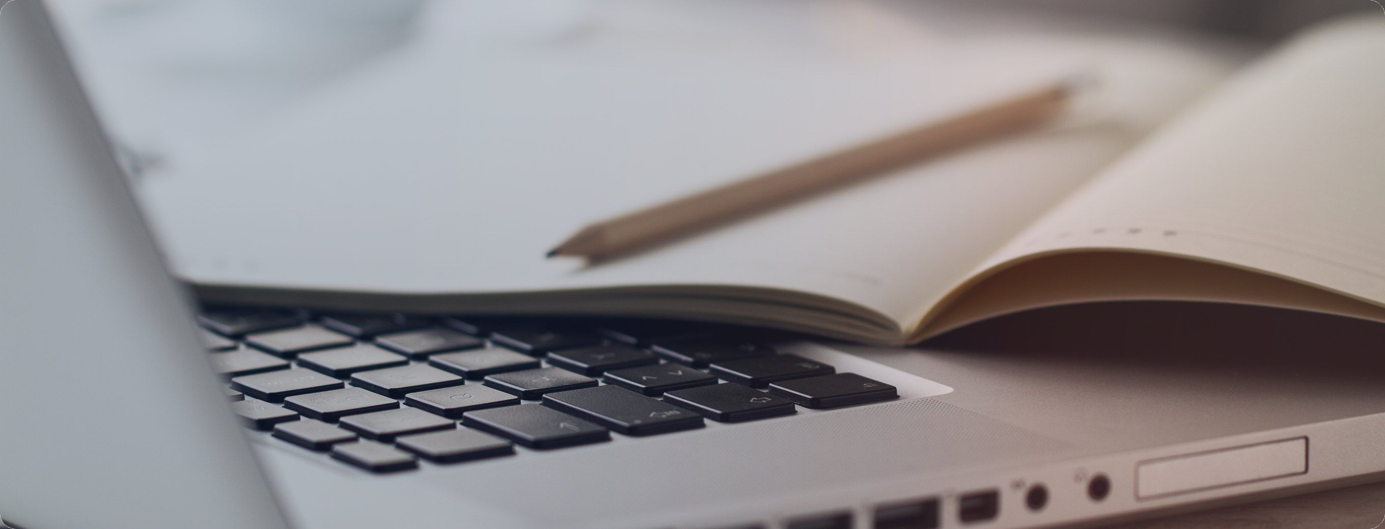 An open notebook and pencil resting beside a laptop keyboard